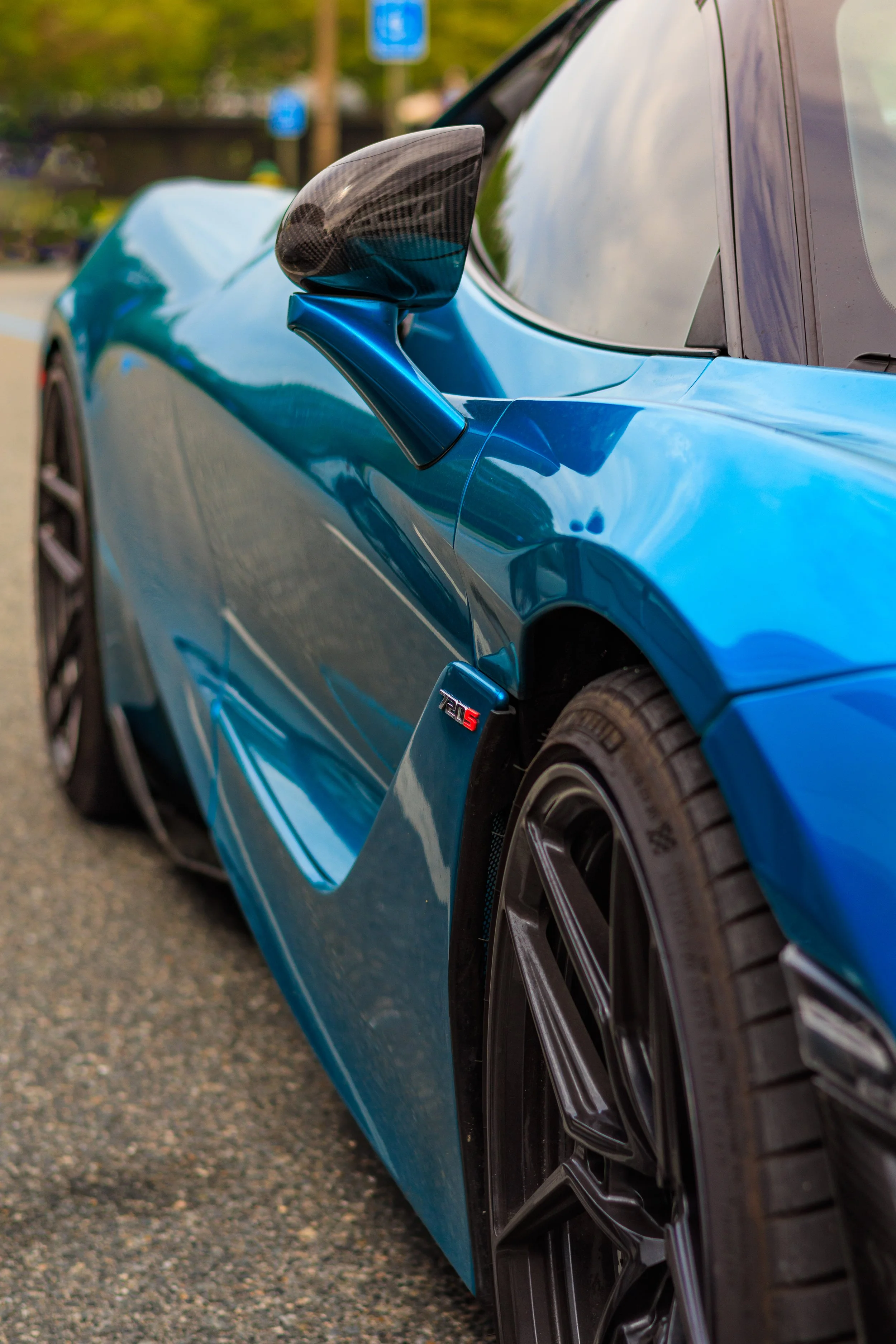 Close-up of a blue sports car, focusing on the side mirror, tire, and badge that reads '720S'.
