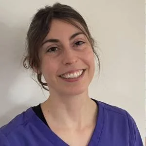 A woman smiling in a blue top against a plain background.