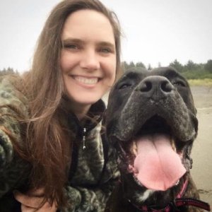 A woman and a large black dog outdoors, both smiling with the woman's arm around the dog.