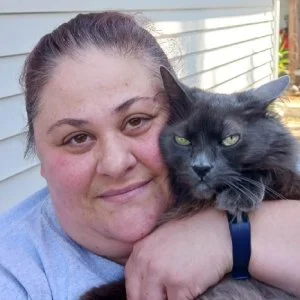 A woman holding a black cat outdoors in front of a white house.