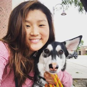 Young woman smiling with a black and white dog outdoors in a parking lot.