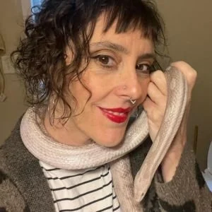 A woman with short curly hair and red lipstick holding a beige snake close to her face.