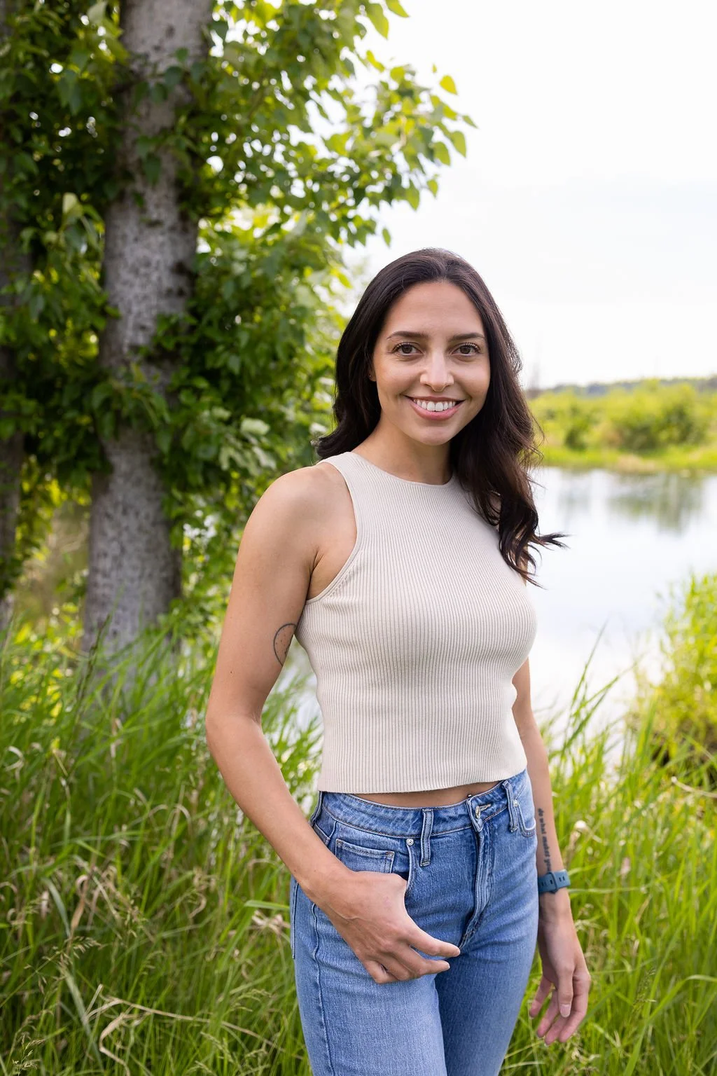 Close-up of a young woman with dark hair smiling outdoors, wearing earrings and a sleeveless top.