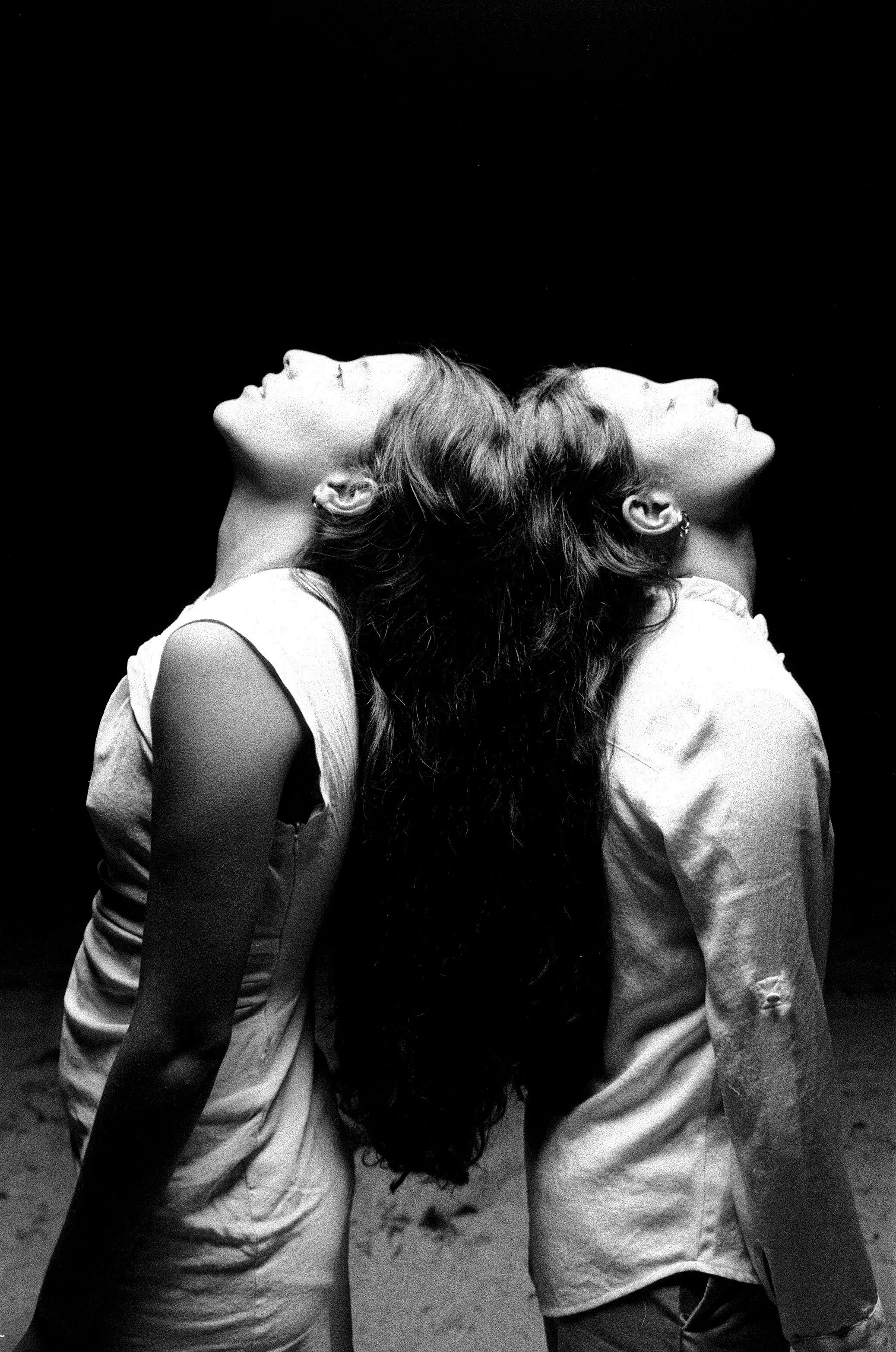 Two sisters stand with their backs to each other , looking up as their long hair hangs down and mesh together.