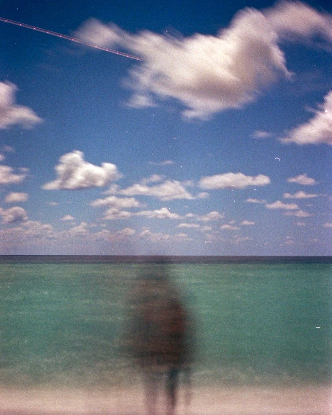 Blurred person standing at ocean shore during cloudy night with a starry sky and a shooting star.