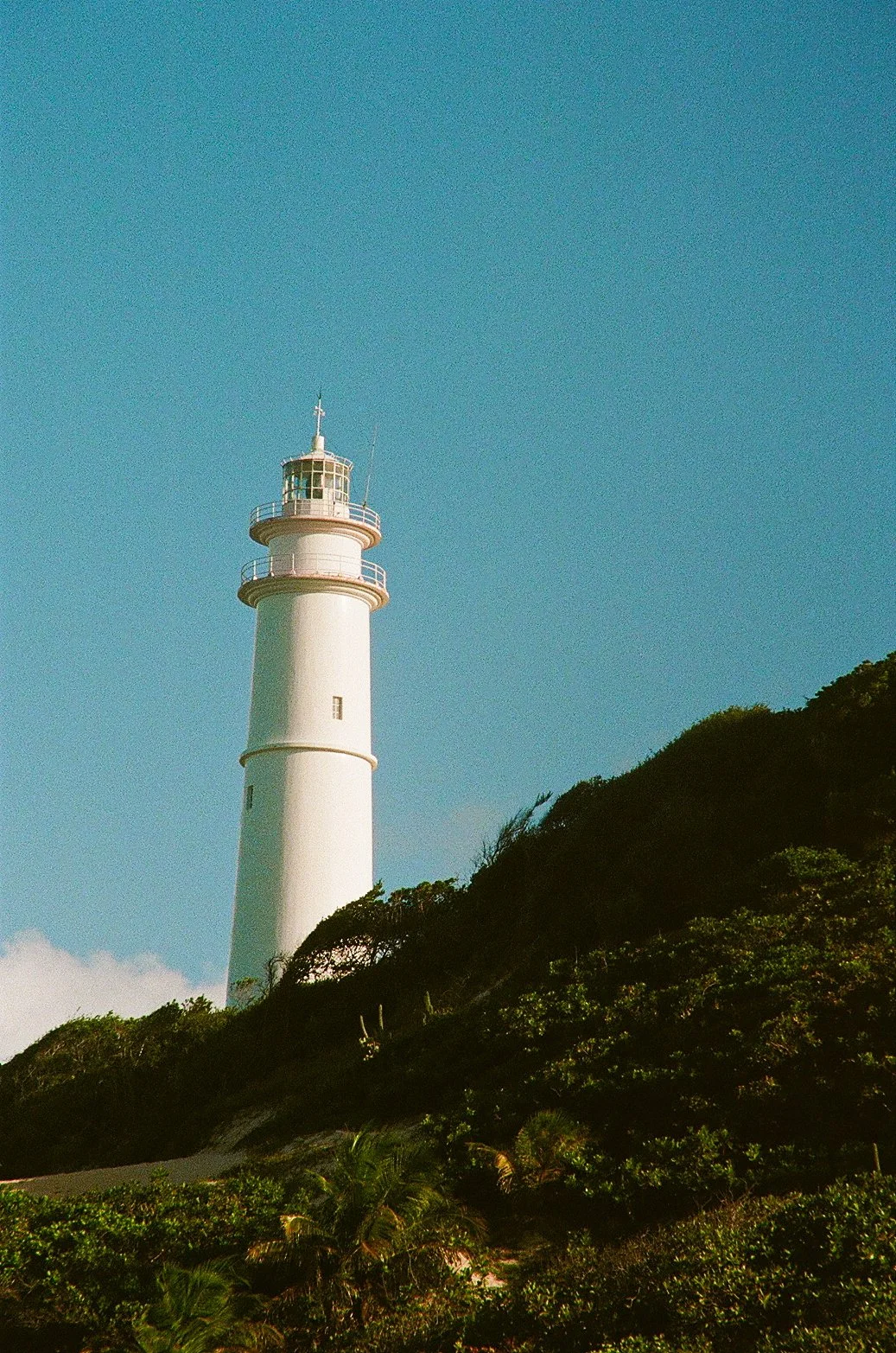 Lighthouse atop a lush green hill and a blue sky in hte background