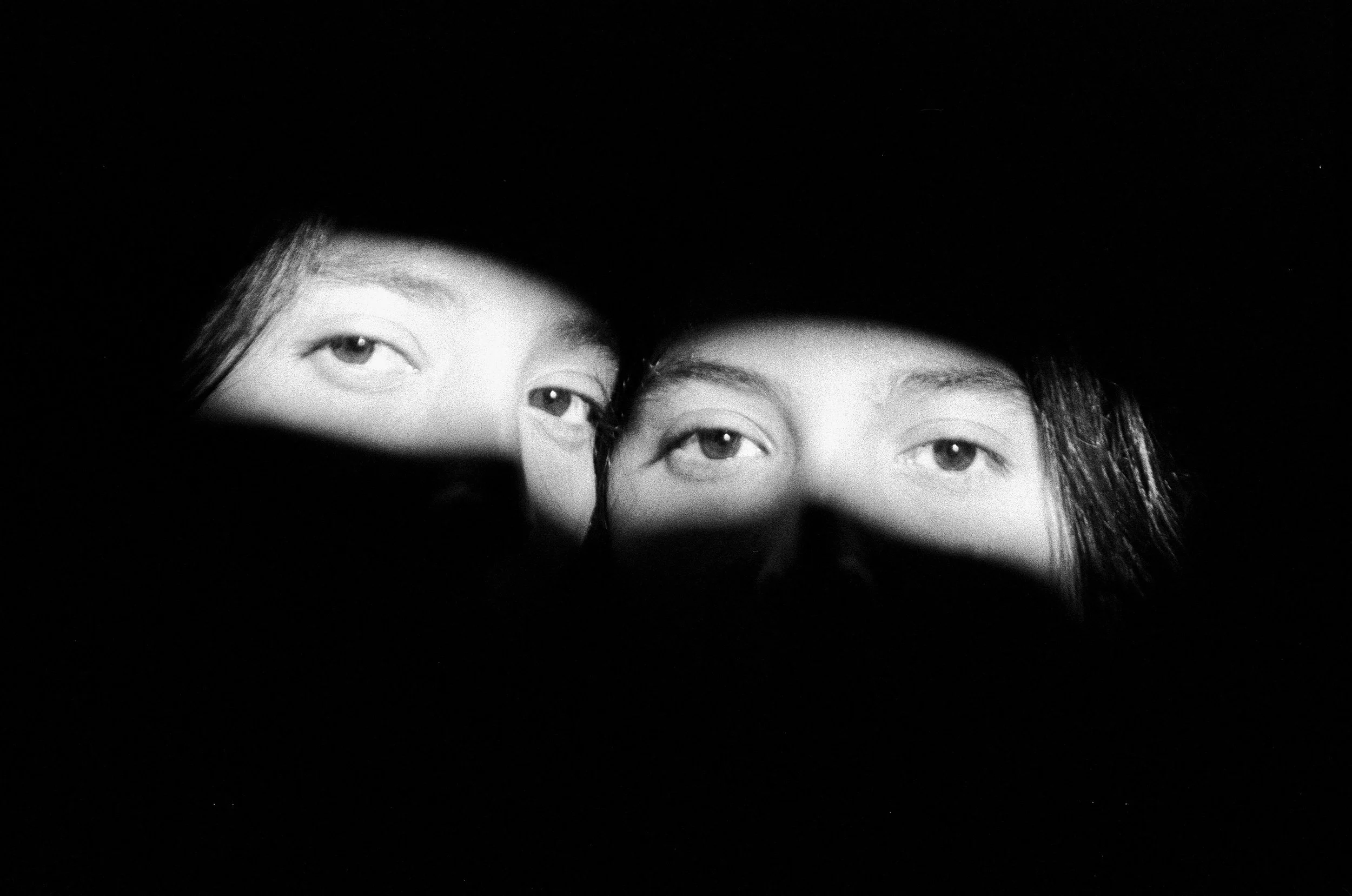 Two sisters look softly at the camera with a stream of light exposing only their eyes.