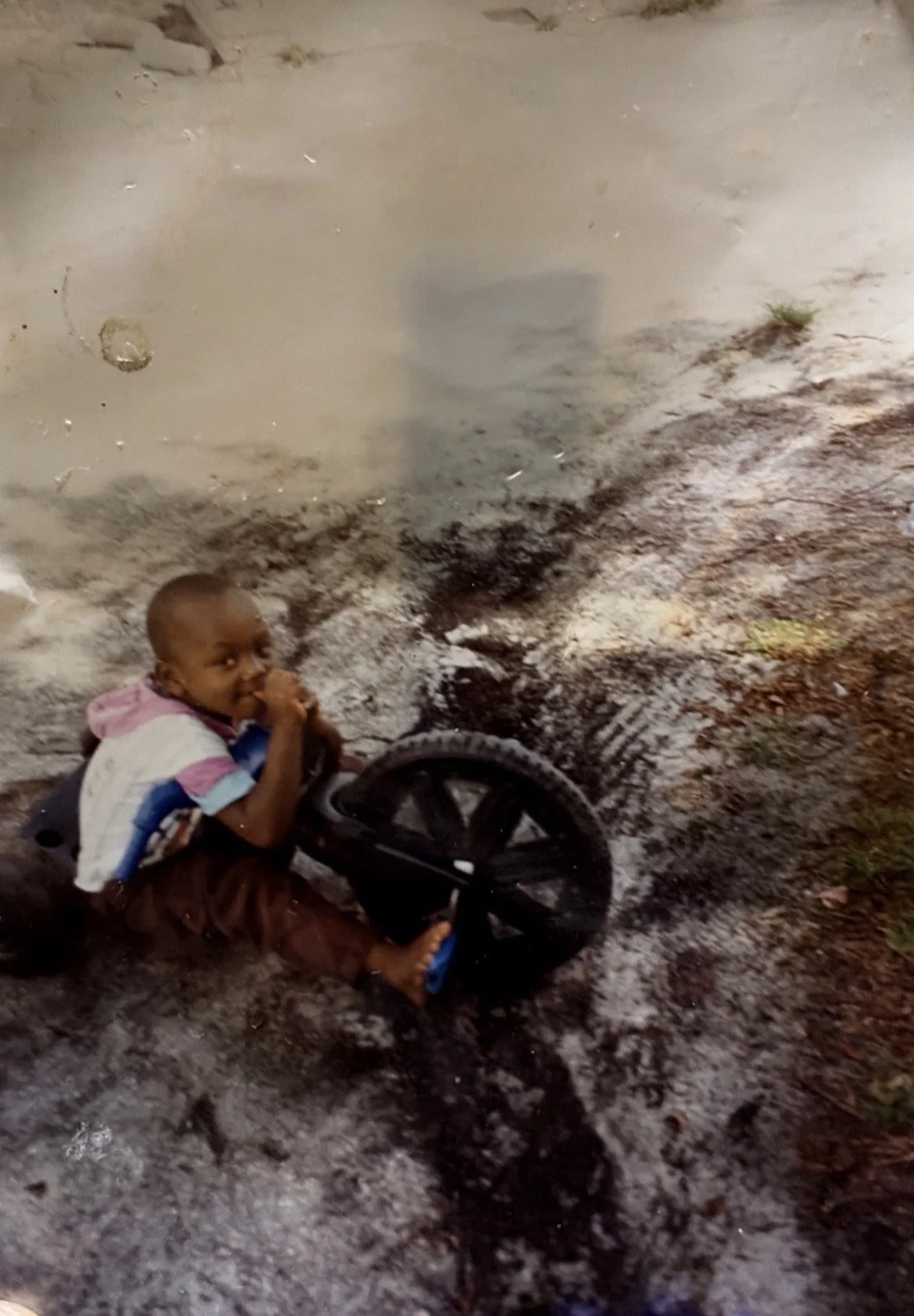 A young boy sits on a "big wheel" toy in a front yard.