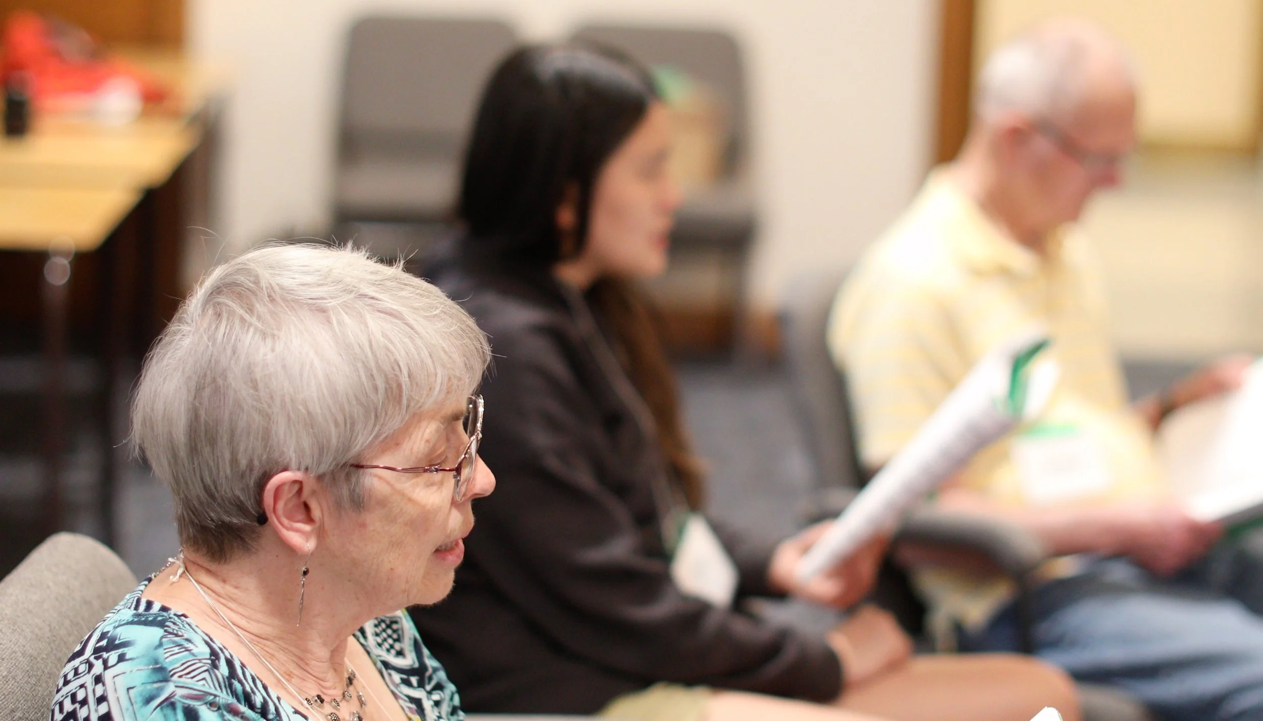 Three people sitting in a row at a meeting or presentation, reading papers or notes.