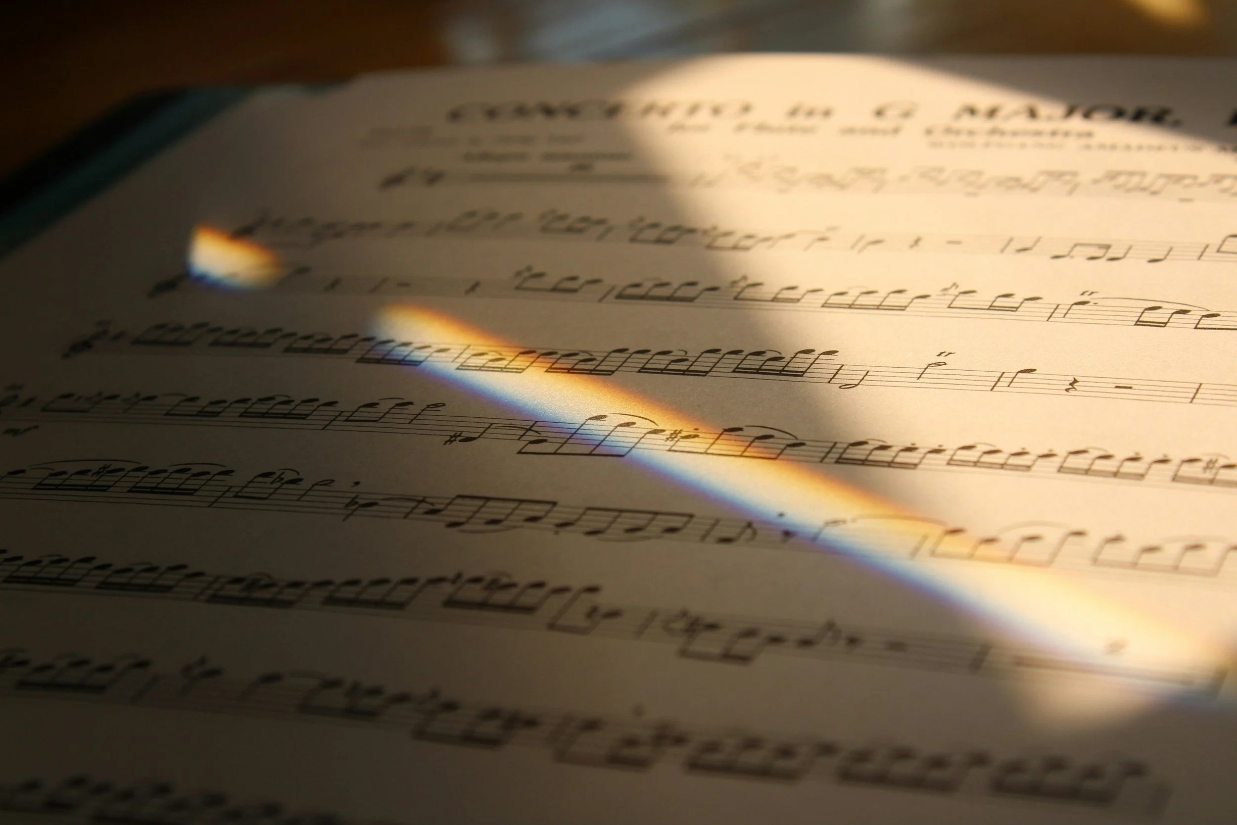 Sheet music illuminated by a rainbow-colored light passing through a glass prism.
