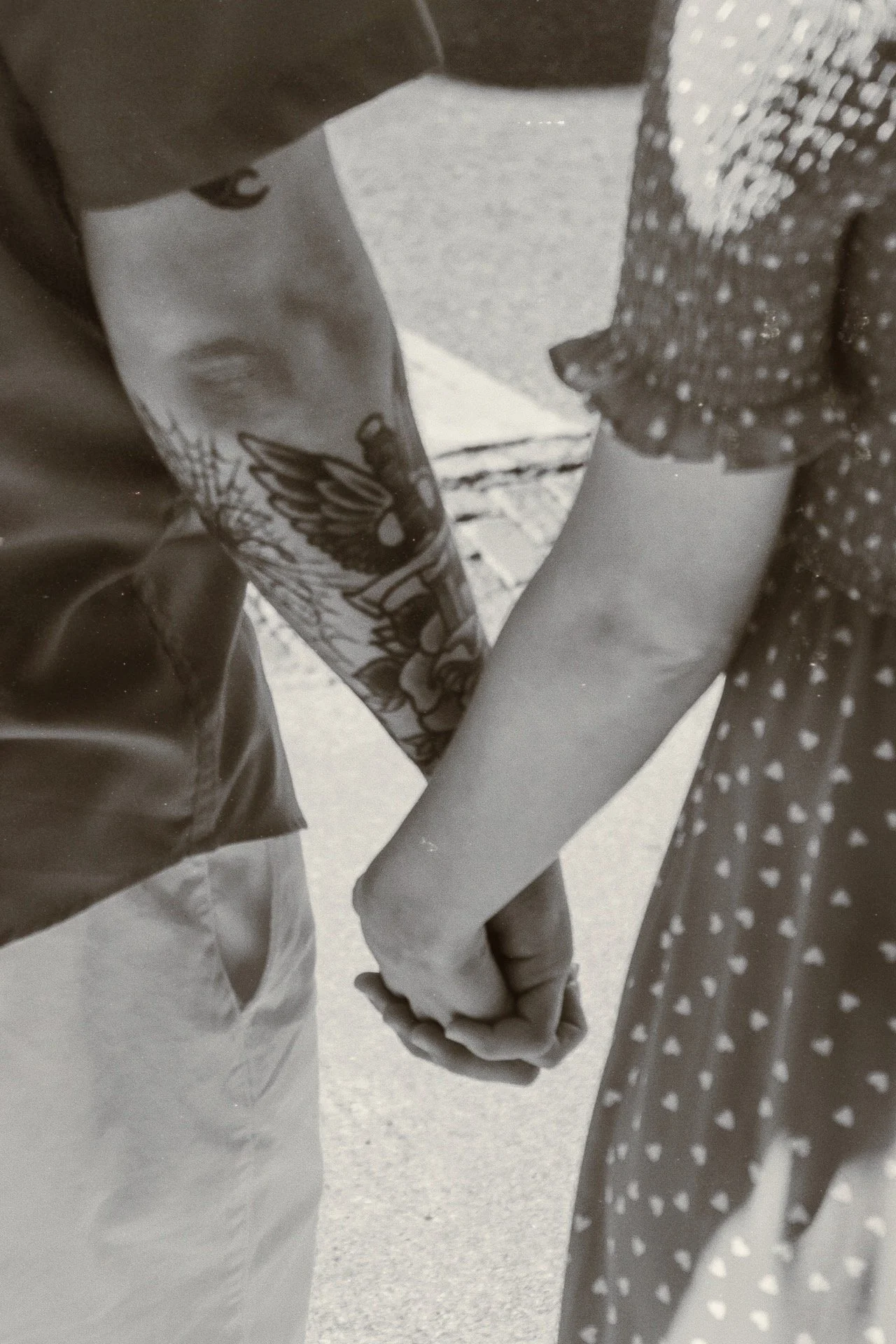 A close-up of two people holding hands, one person's hand with tattoos and the other's hand resting on the other's palm, with part of their clothing visible.