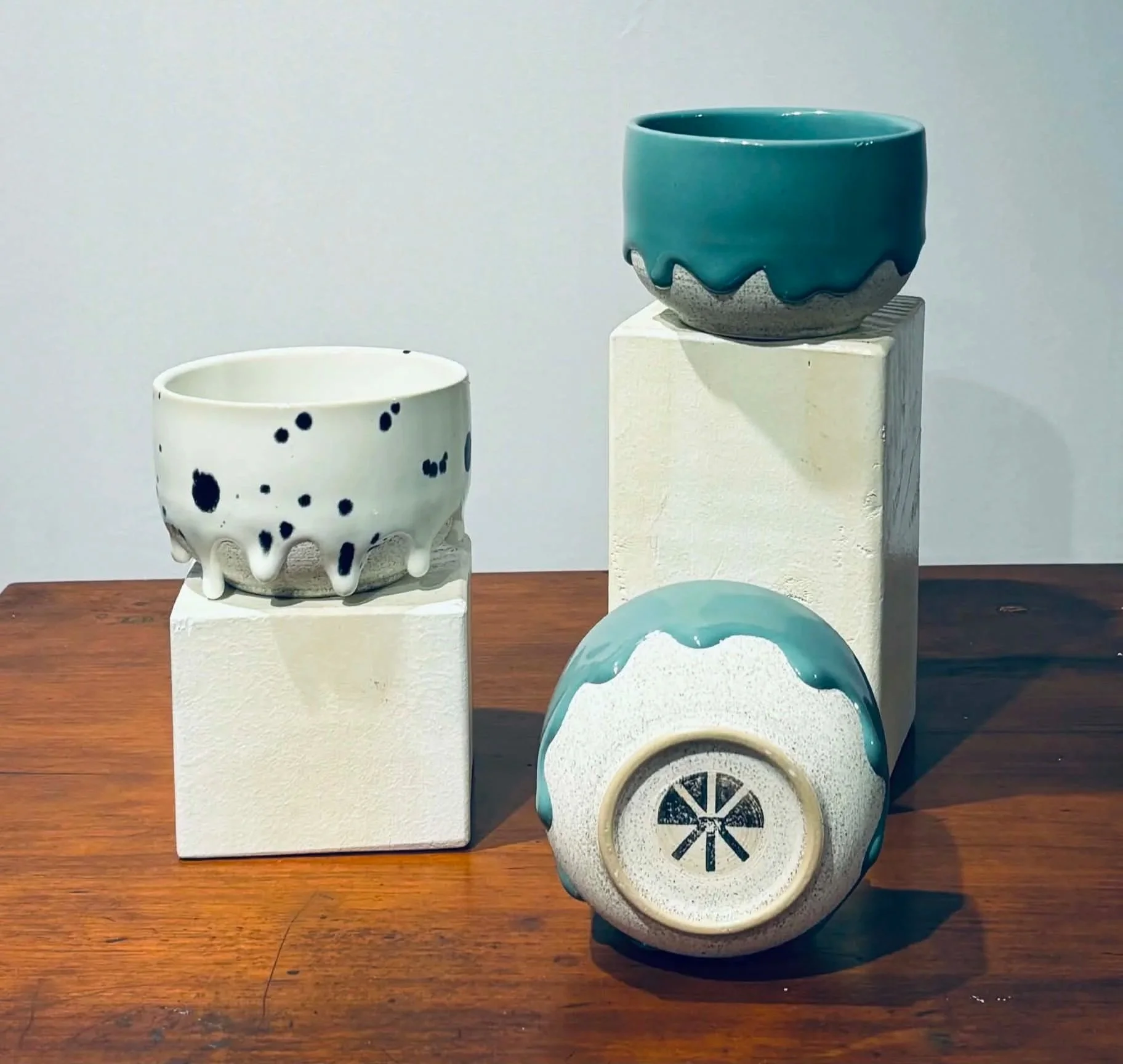 Collection of ceramic bowls with different designs and colors on white pedestals, displayed on a wooden surface.