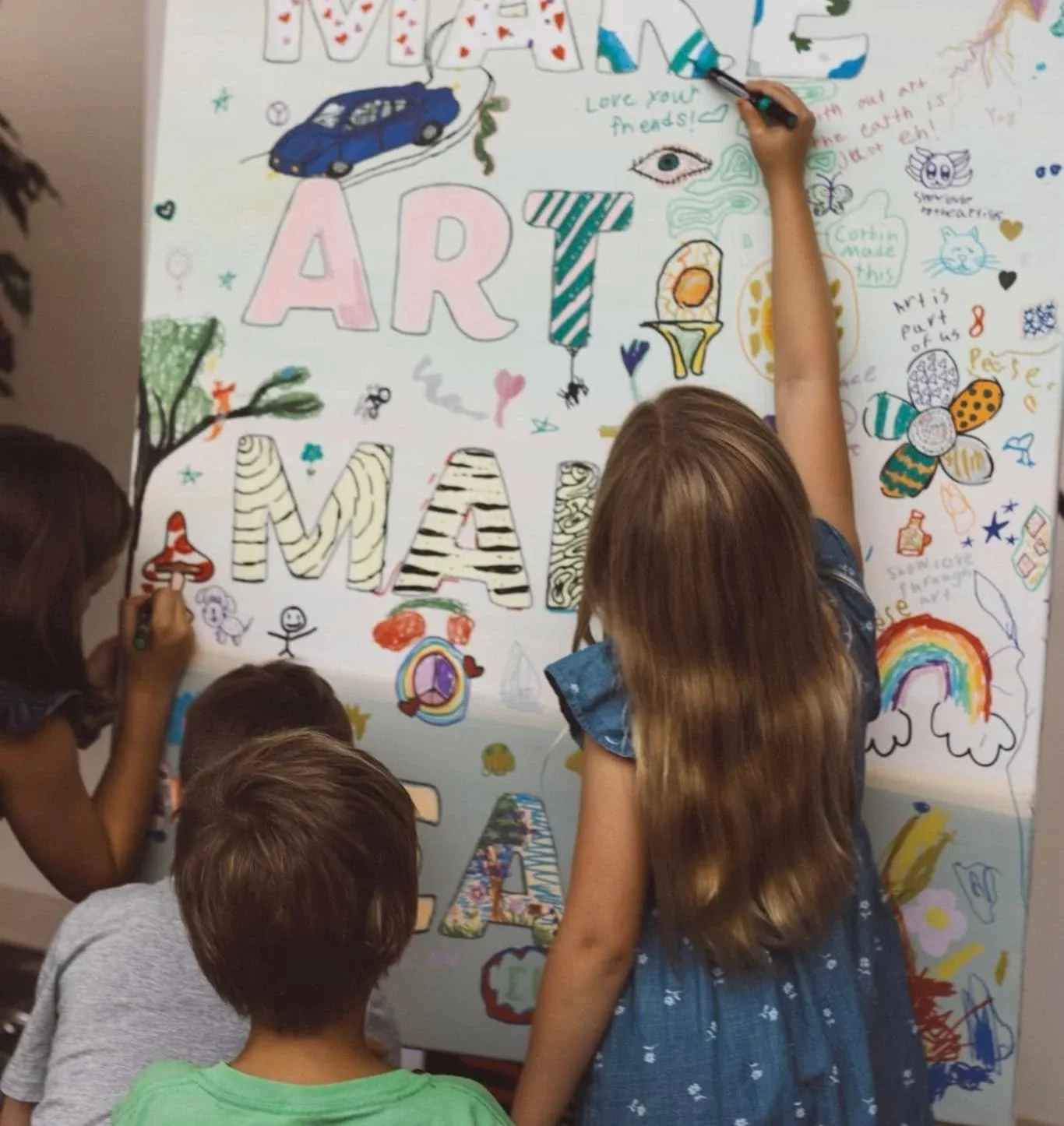 Children drawing on a large white poster with colorful letters and illustrations.