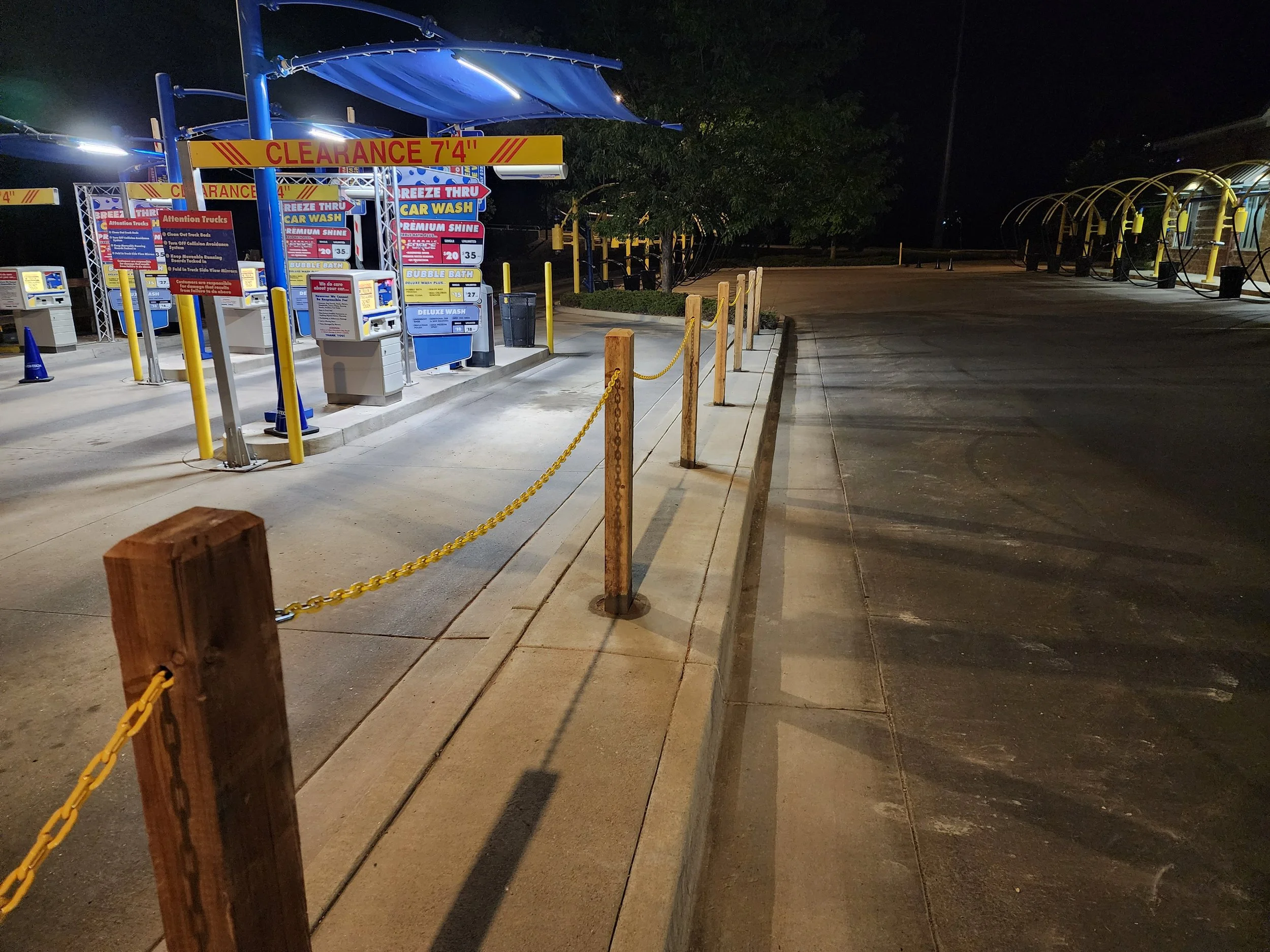 An empty car wash parking lot at night with signs and a yellow chain barrier.