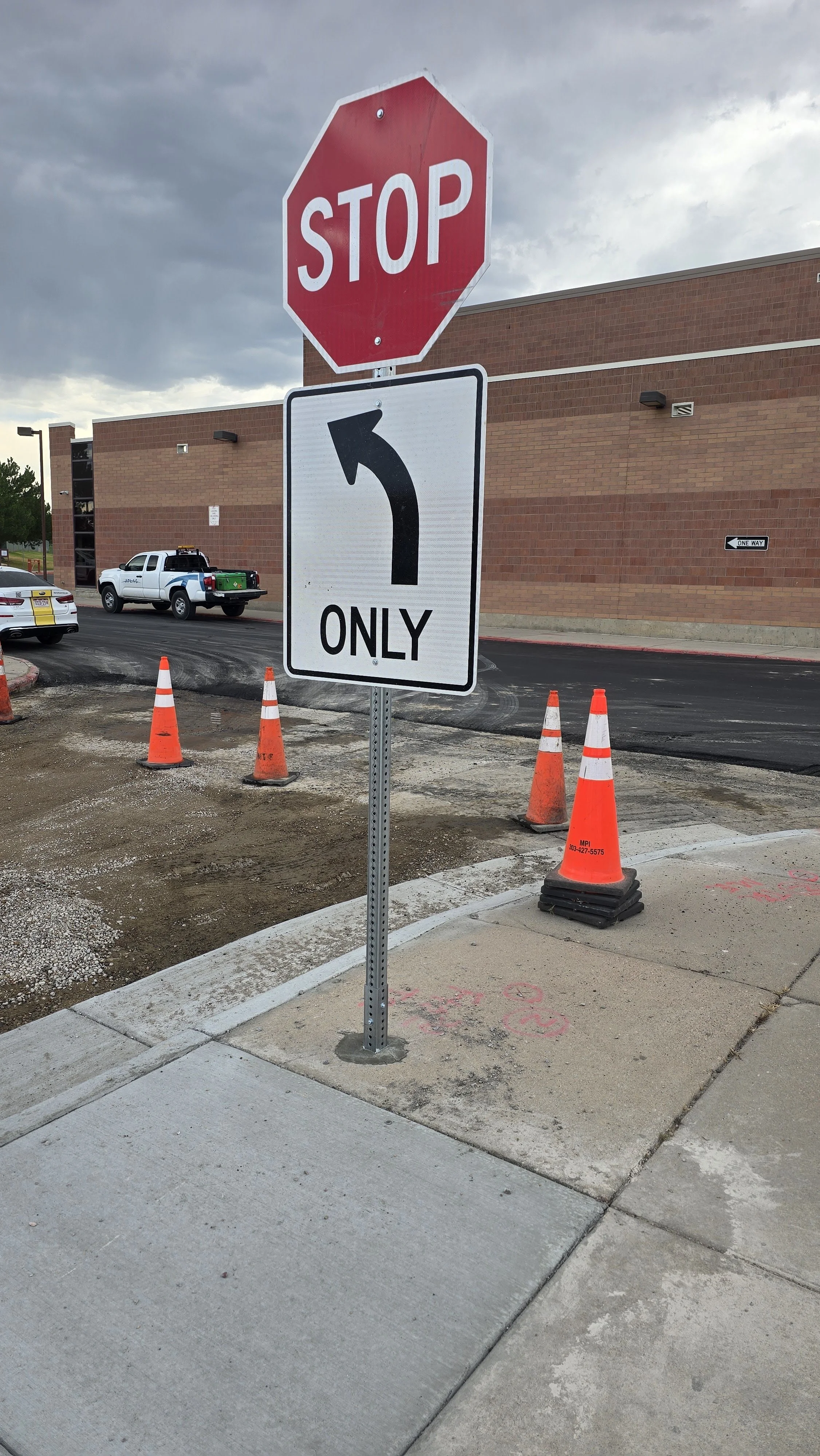 Stop sign and left turn only traffic sign at a construction zone, with orange cones and a brick building in the background.