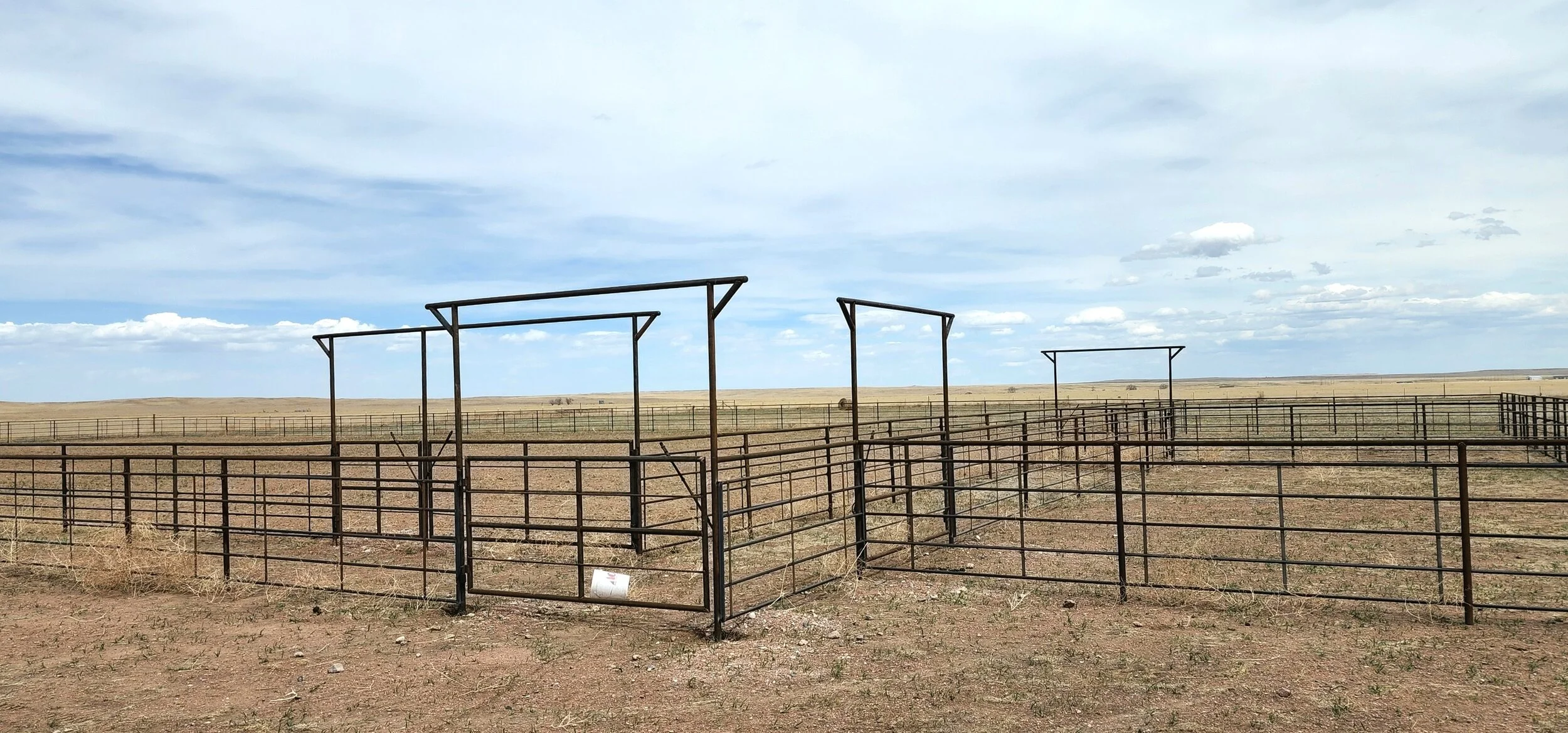 A fenced-off corral structure in an open, flat, rural landscape under a cloudy sky.