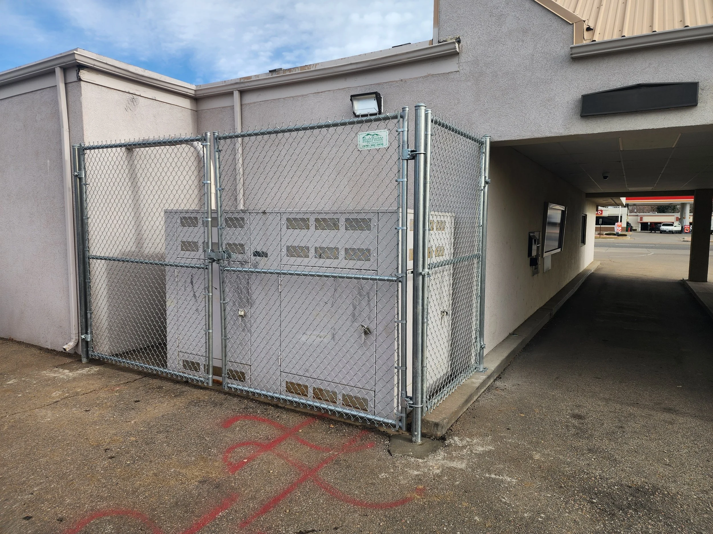 Fenced utility box outside on a building wall, with an alley and parking lot in the background.