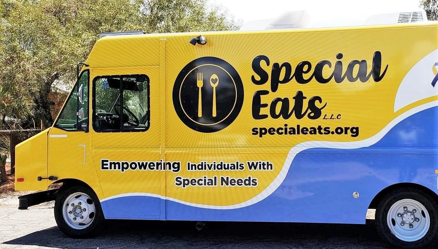 Yellow and blue food truck with the logo and name 'Special Eats LLC' and the website 'specialeats.org' on the side, along with the slogan 'Empowering Individuals With Special Needs.'