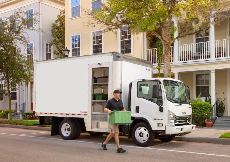 A man unloading a green plastic storage bin from a white moving truck parked on a residential street.