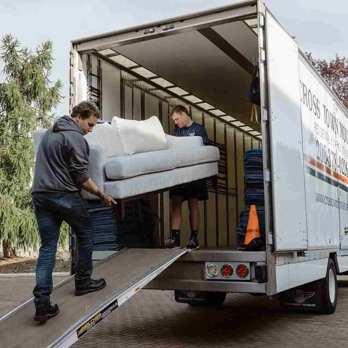 Two men unloading furniture from a moving truck, with one man carrying a couch and the other inside the truck.”}