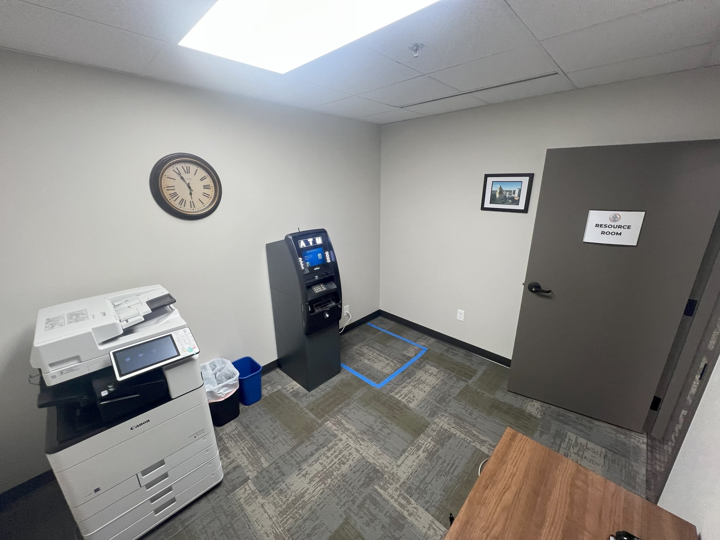 Office resource room with a wall clock, a photocopier, an ATM machine, and a door labeled 'Resource Room'.