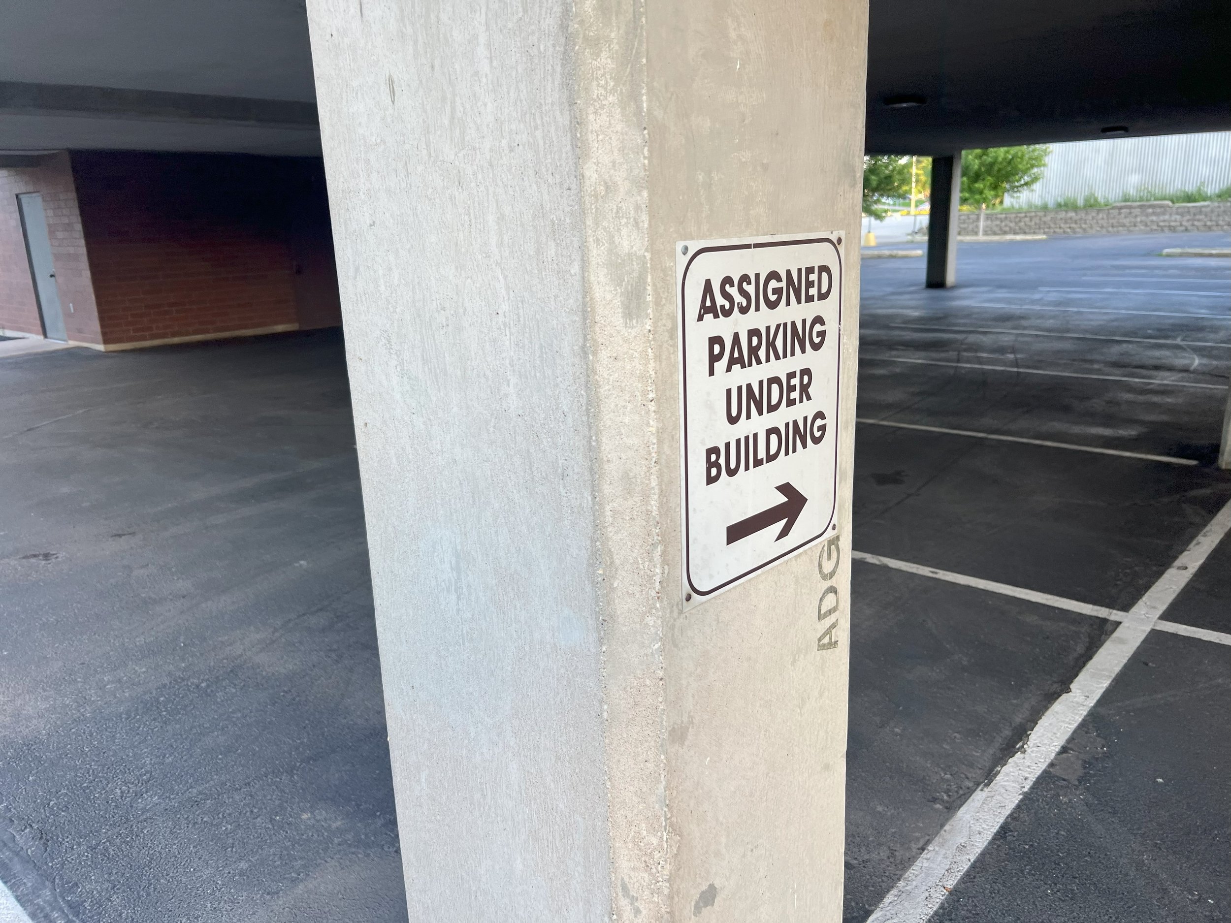 Sign on concrete pillar with arrow pointing right saying 'Assigned Parking Under Building'