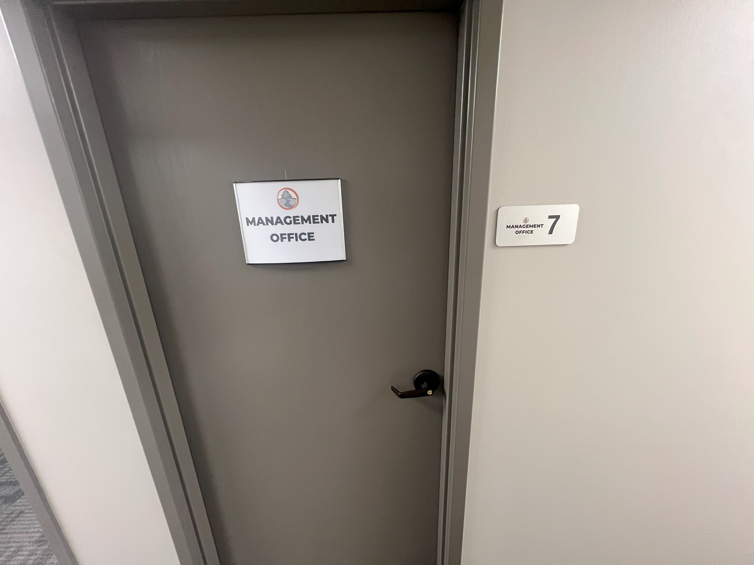 Gray door with a sign that reads Management Office, next to a wall-mounted sign with the number 7 and the words Management Office.