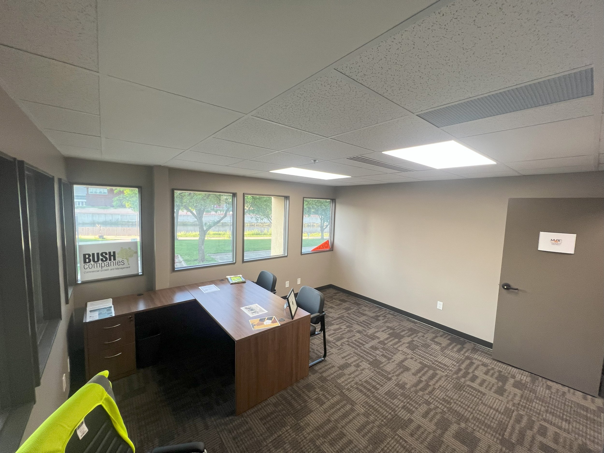 Empty office with a desk, three chairs, and a window view of trees and grass outside.