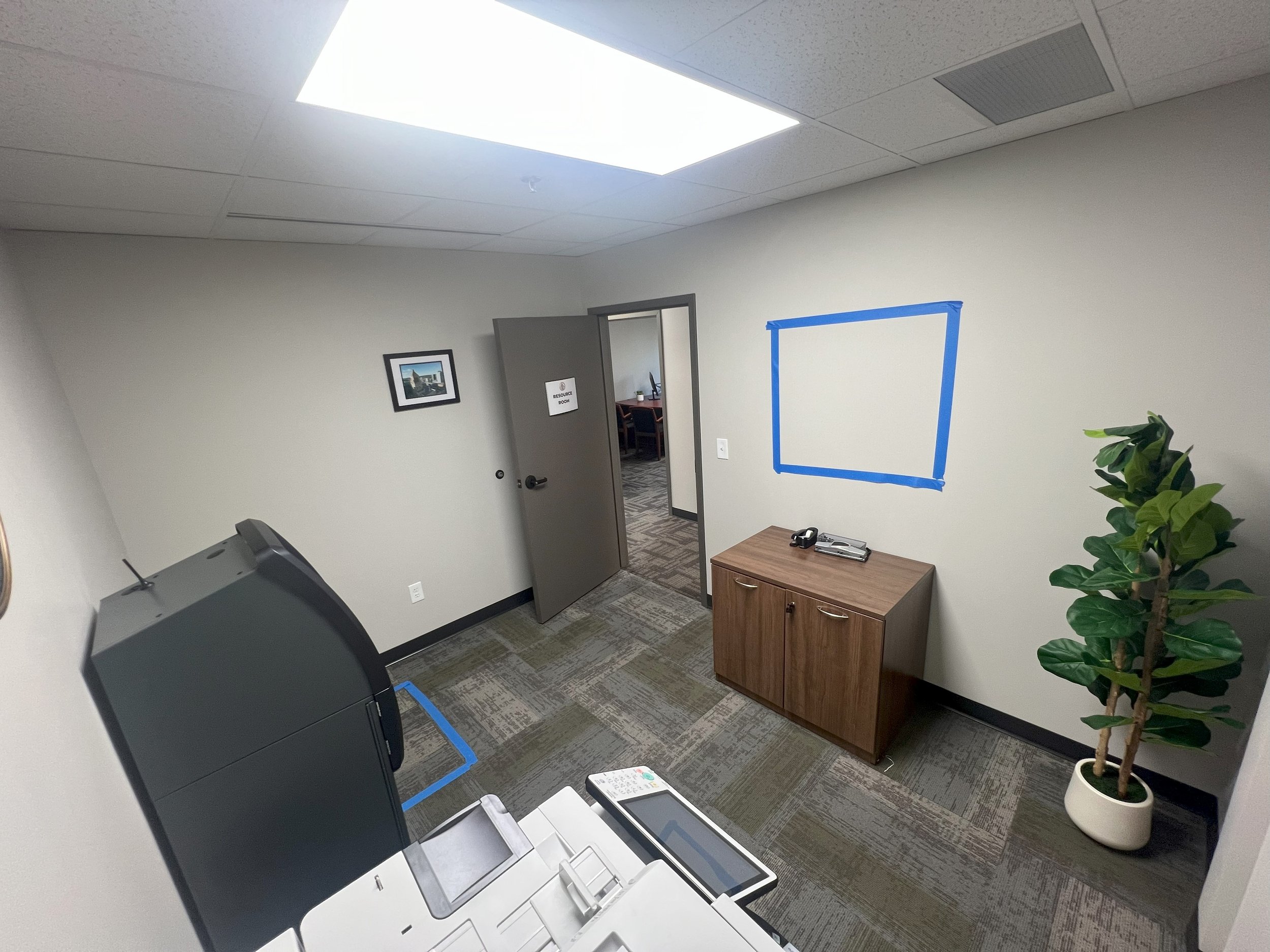 Empty office room with a door, desk, potted plant, and a blue square on the wall.