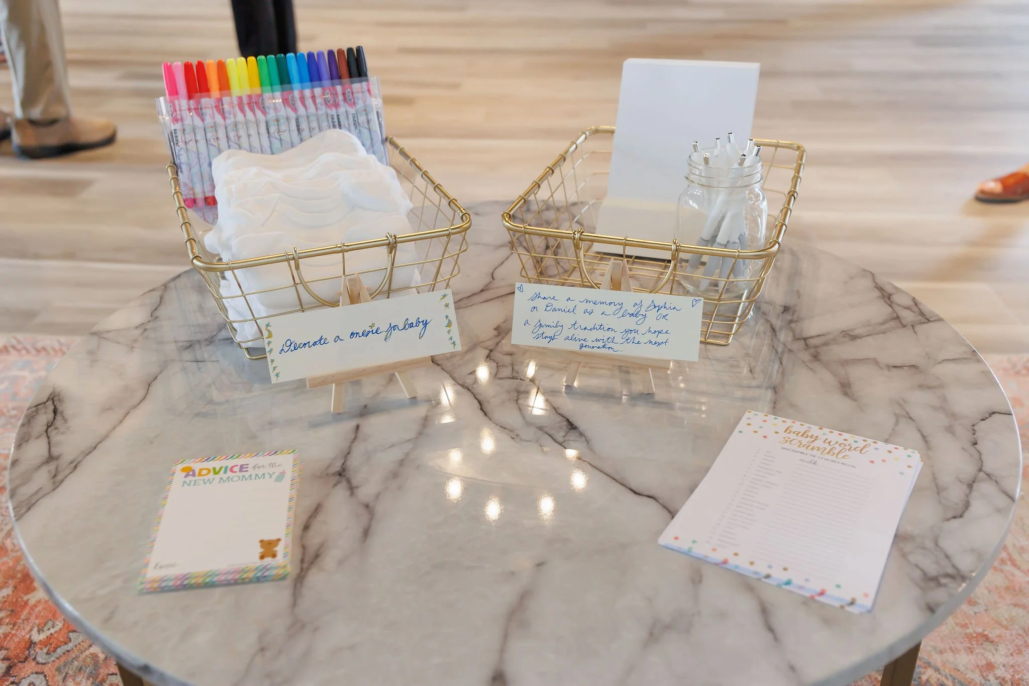 Wedding or baby shower guest sign-in table with markers, pens, and personalized signs, on a round marble table.