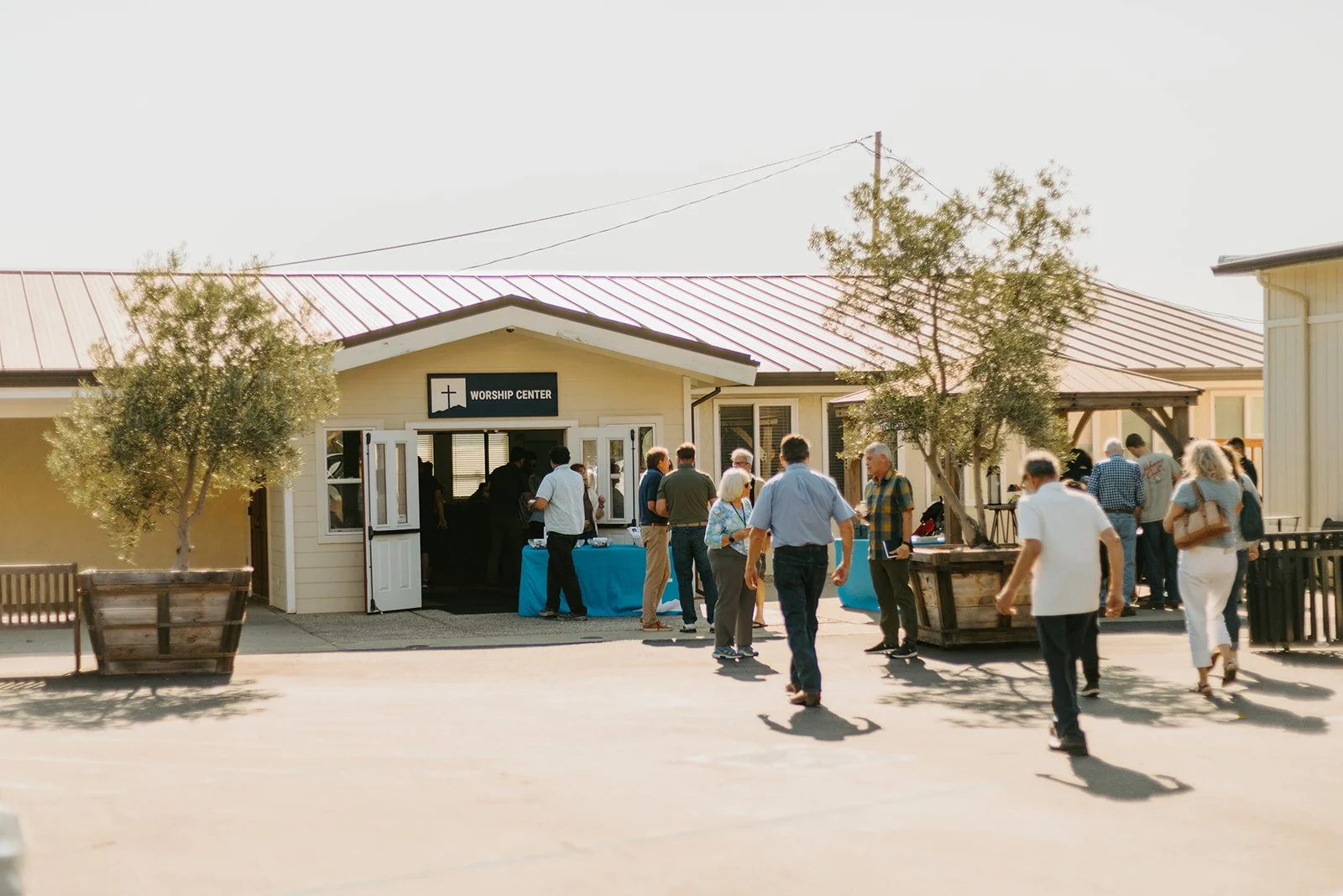 People gathering outside a worship center with a sign that says 'Worship Center,' under a sunny sky.