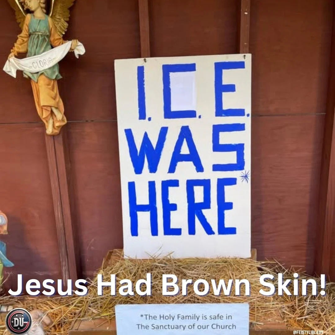 A religious display features a white sign with blue letters reading 'ICE WAS HERE' in a vertical arrangement, leaning against a wooden wall. To the left, a religious statue of Jesus with a halo and flowing robes is visible. The display is set on hay, and a small sign with text about the Holy Family is also present.
