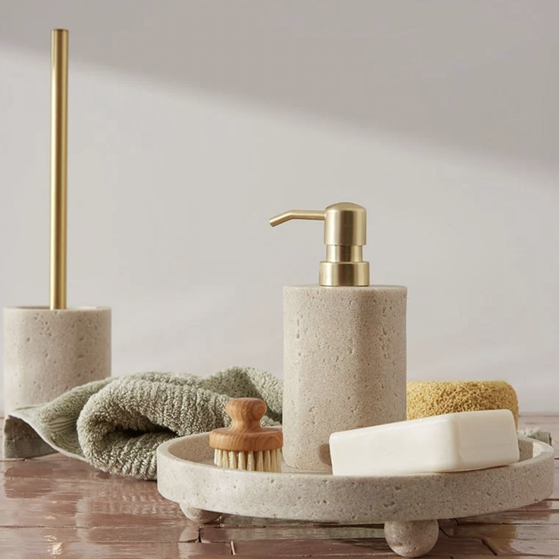 Bathroom accessories including a soap dispenser, brush, soap, and a towel on a circular tray.