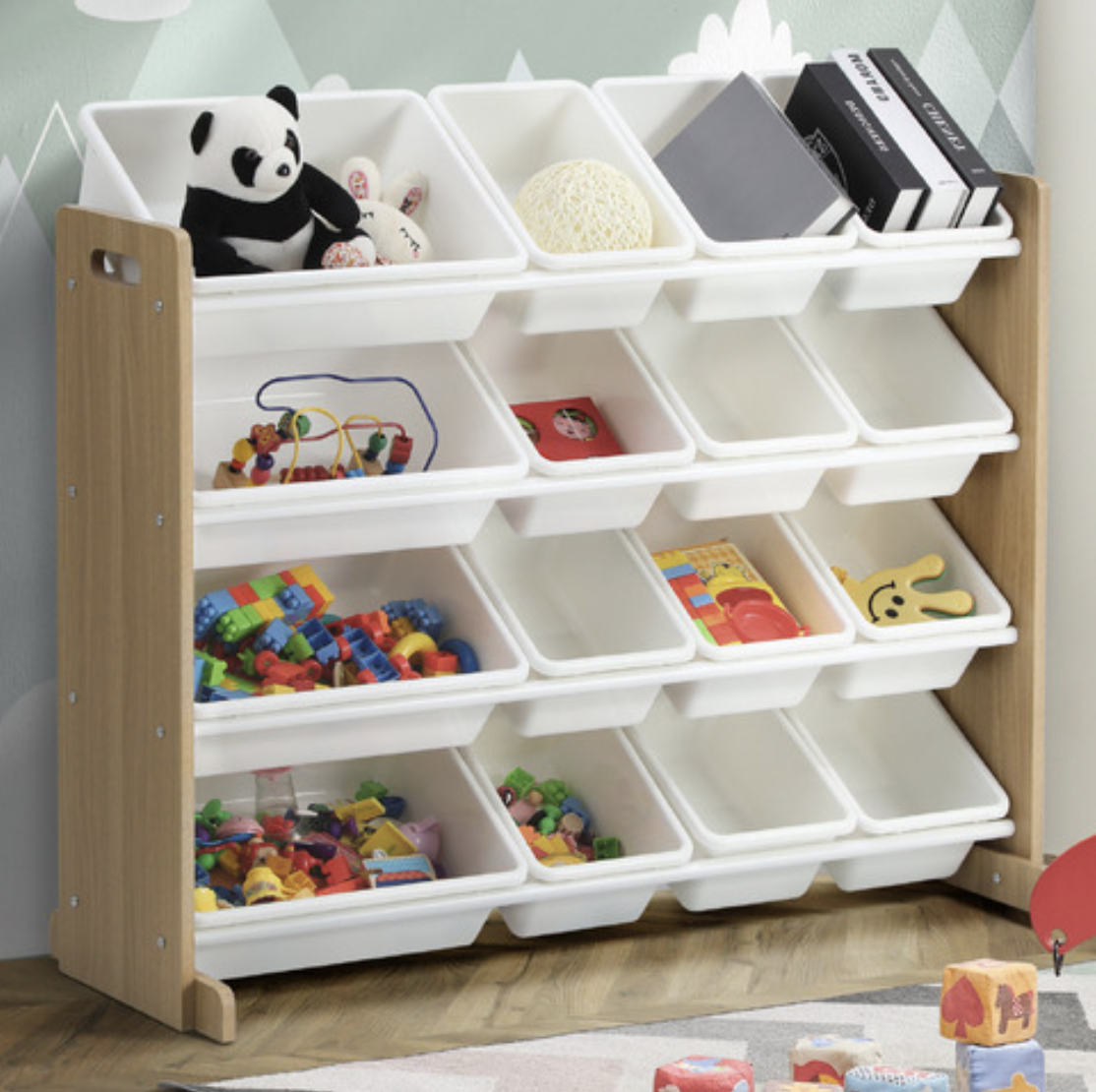 A wooden toy storage shelf with white bins filled with toys, including a panda stuffed animal, a yellow sponge, books, Lego bricks, and wooden toys. Small toys are on the floor in front of the shelf.
