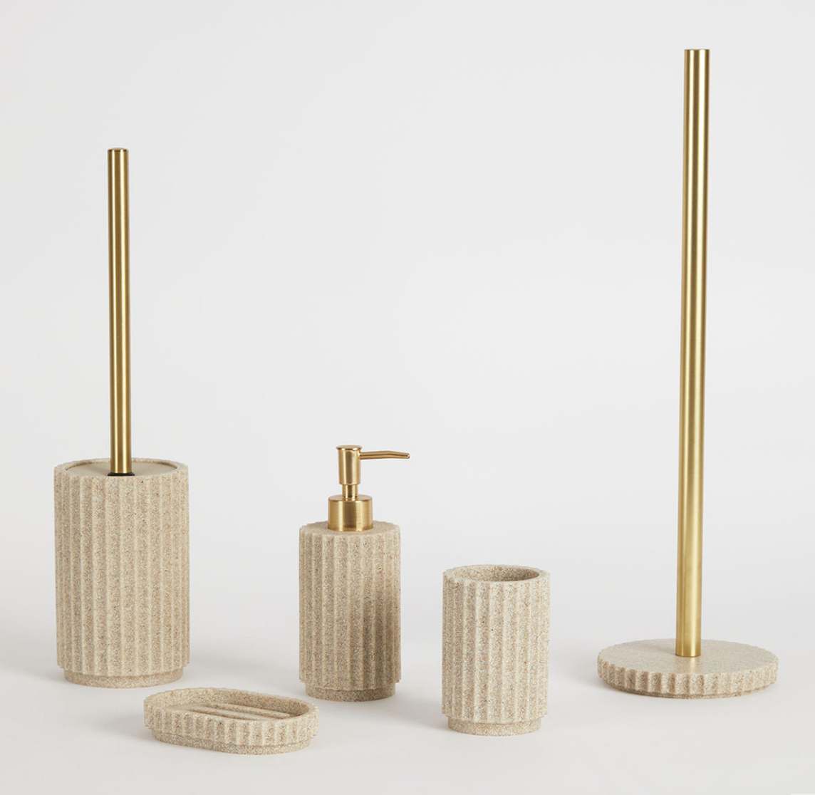 Set of four bathroom accessories with gold accents and textured beige bases, including a toilet brush holder, soap dispenser, tooth brush holder, and towel stand