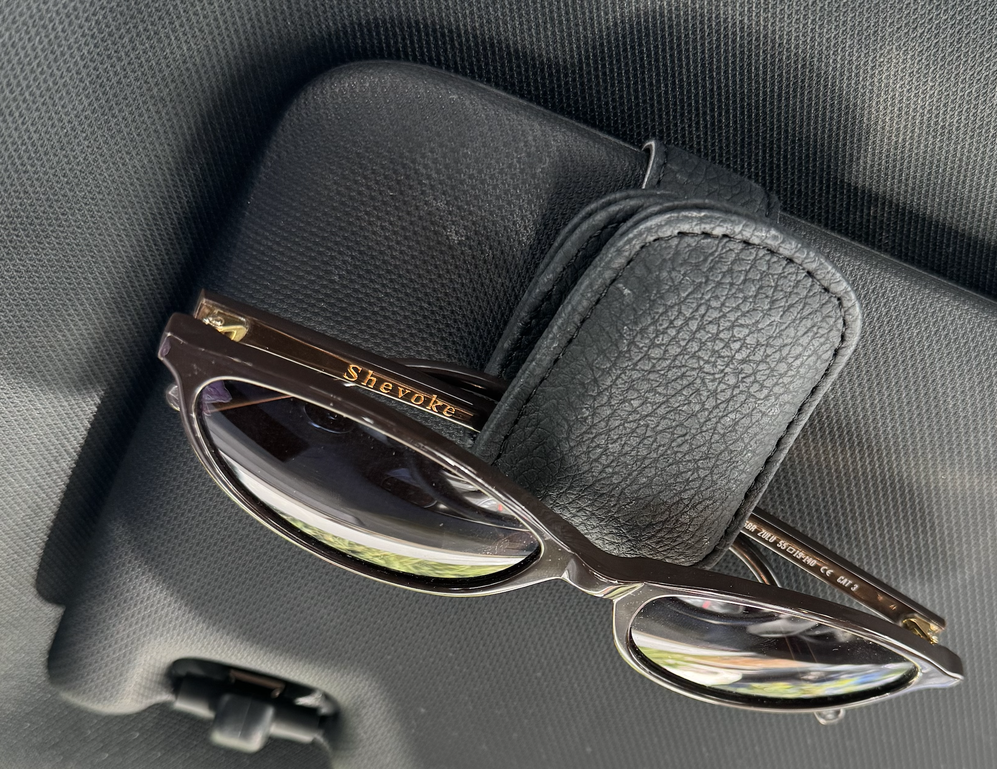 A pair of sunglasses with a black case inside a car, placed on a gray surface.