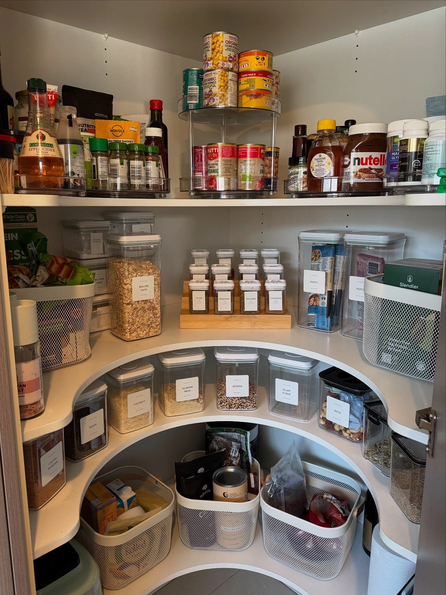 A well-organized pantry with shelves containing canned goods, jars of spices, and containers of grains, pasta, and snacks in clear containers with labels.