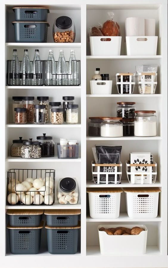 Pantry shelves with labeled jars, baskets, and containers holding snacks, spices, canned goods, and produce like onions and potatoes.