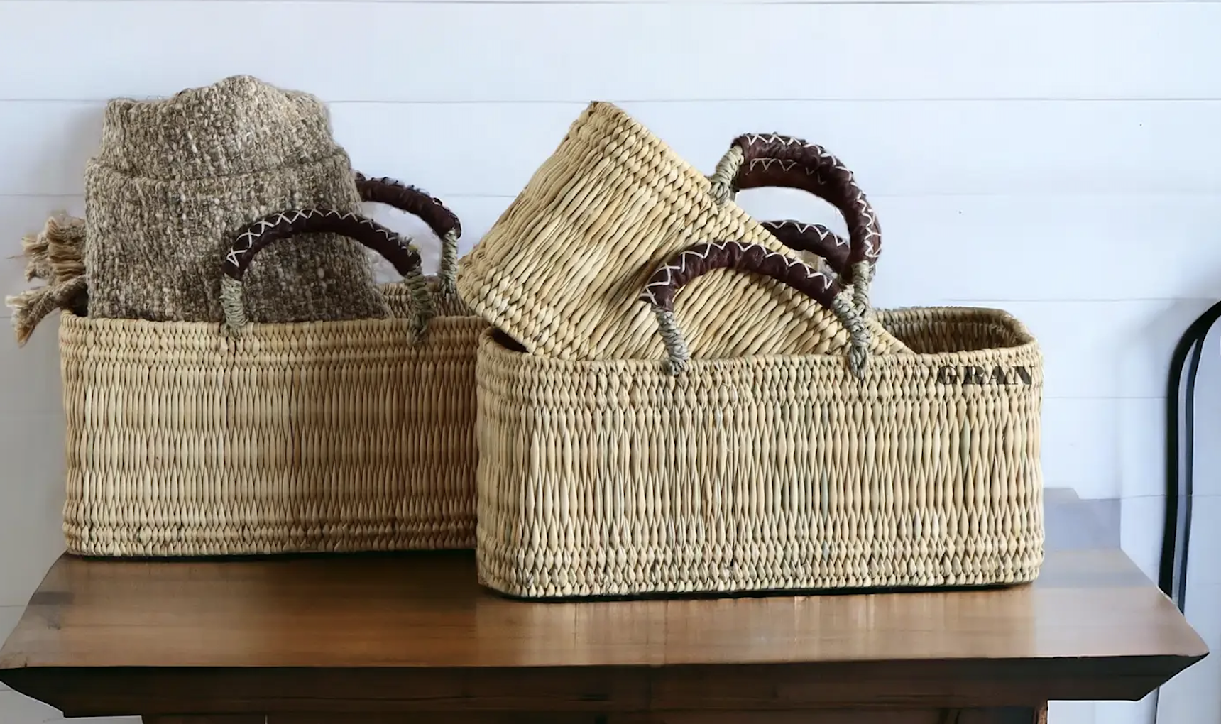 Two woven baskets containing folded textiles are placed on a wooden table against a white wall.