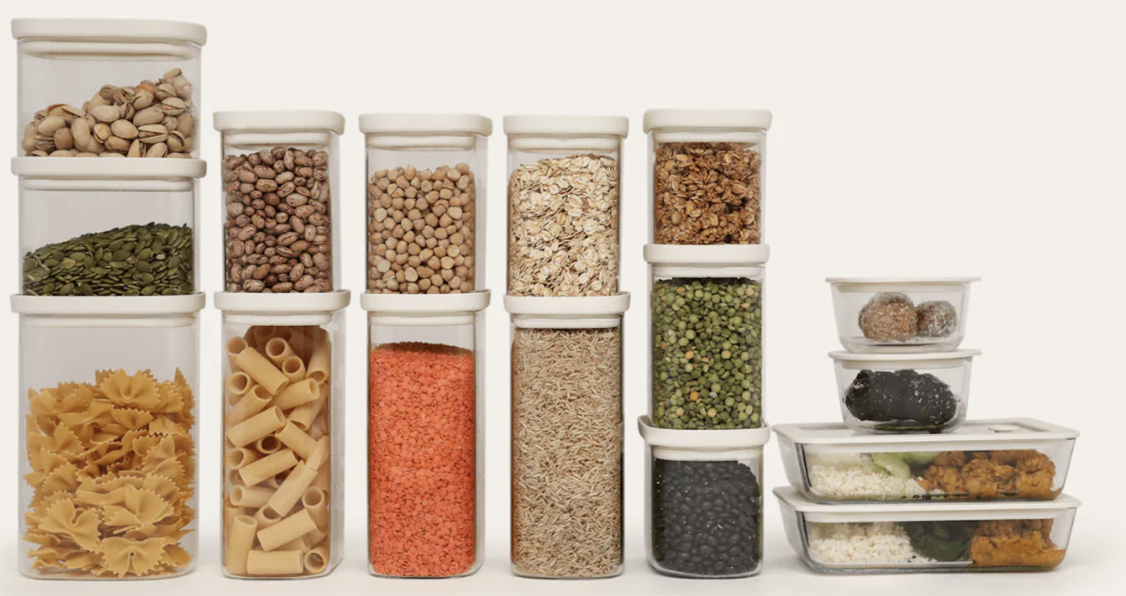 Various dry food items in clear plastic containers, including pasta, grains, seeds, and snacks, arranged in a grid pattern.
