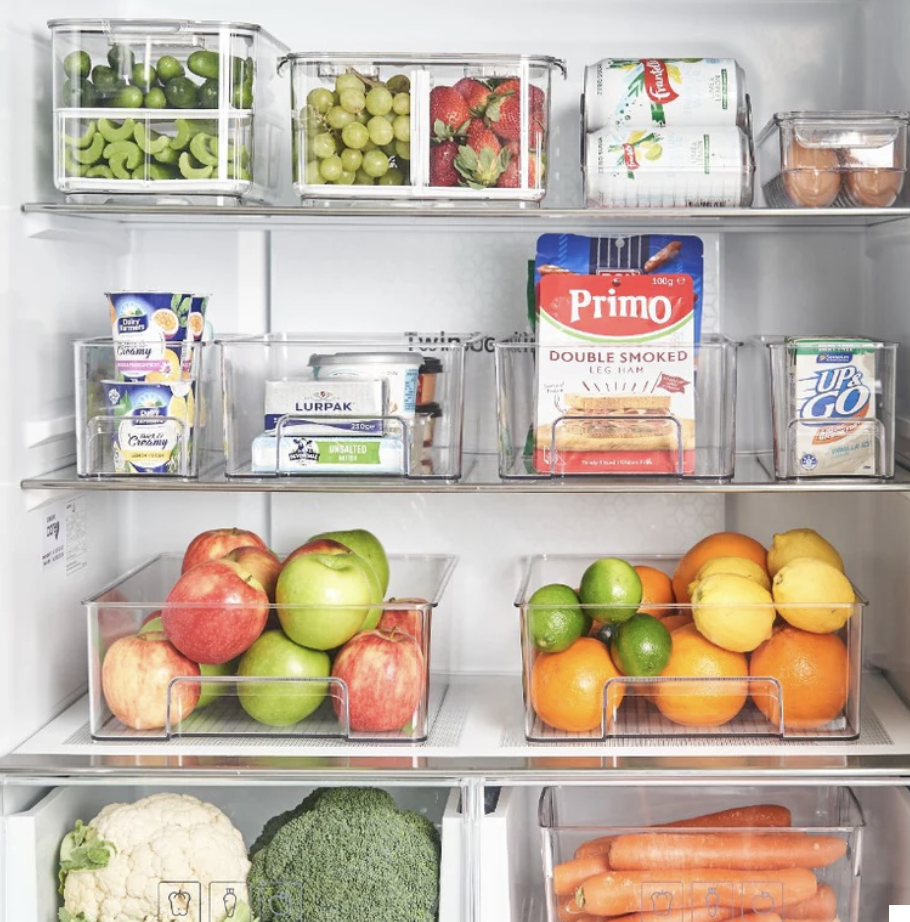 Inside of a refrigerator with multiple clear storage containers containing fruits, vegetables, dairy products, eggs, and packaged food items.