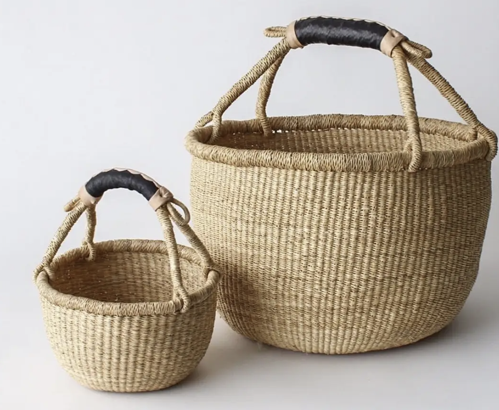 Two woven baskets with black leather handles placed against a plain white background.