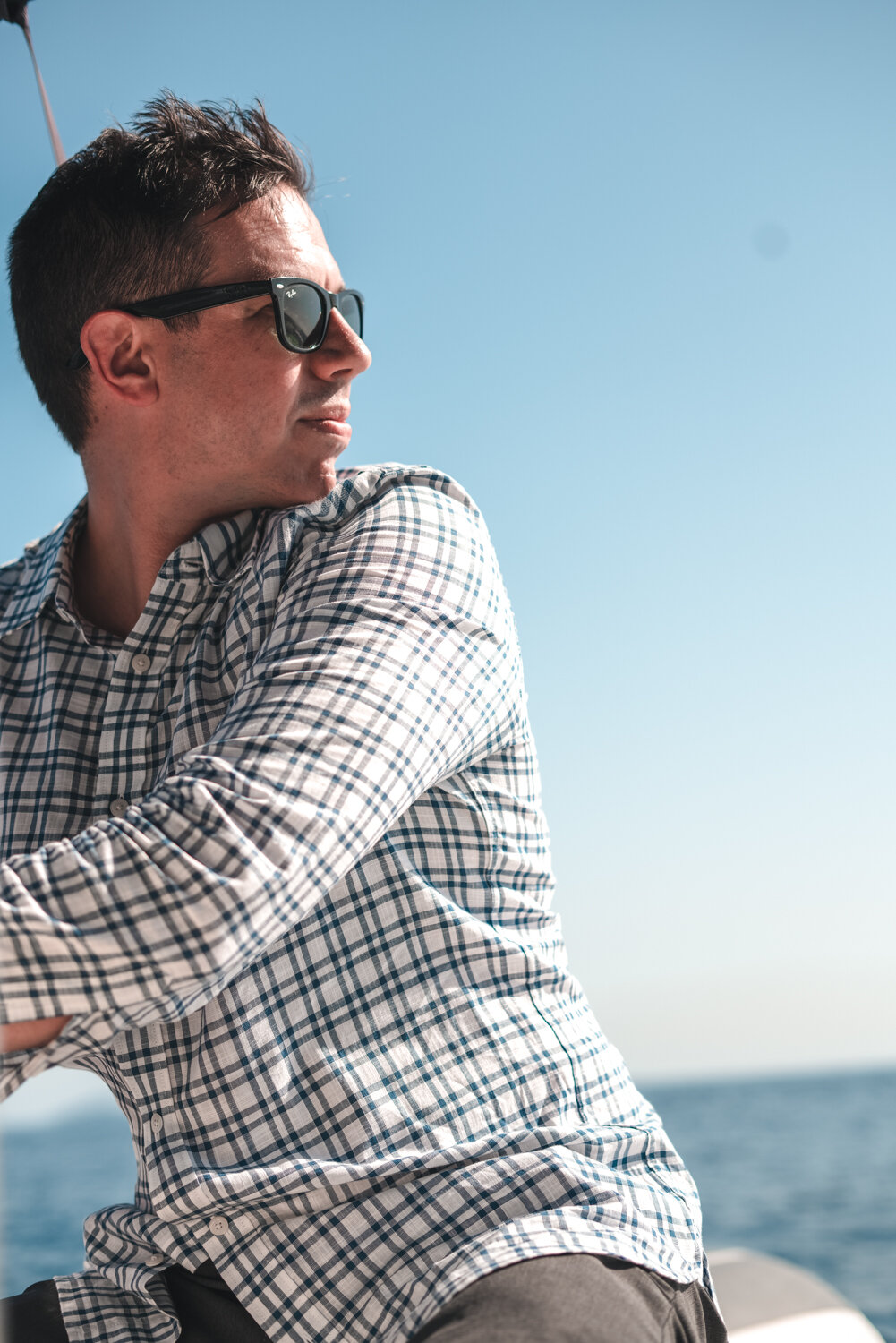 Meditator, commercial realtor, and attorney, Rick Fabiani II, wearing sunglasses and a plaid shirt piloting a boat with an ocean in the background under a clear blue sky.
