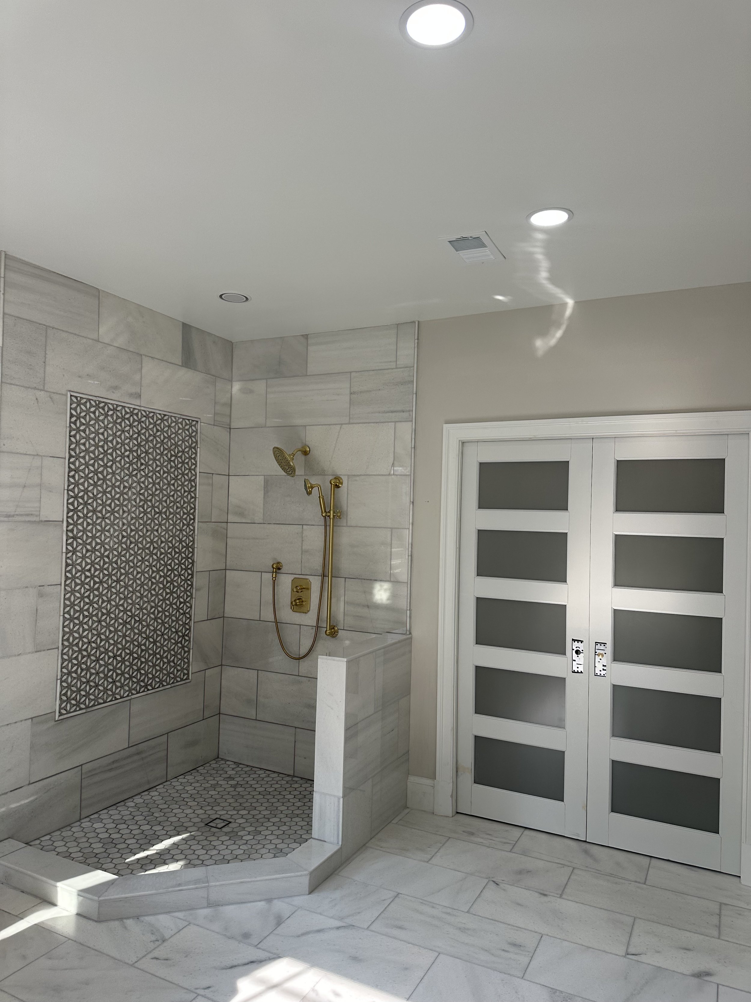 Luxury shower area with gold fixtures, gray tile walls, and a sliding frosted glass door.