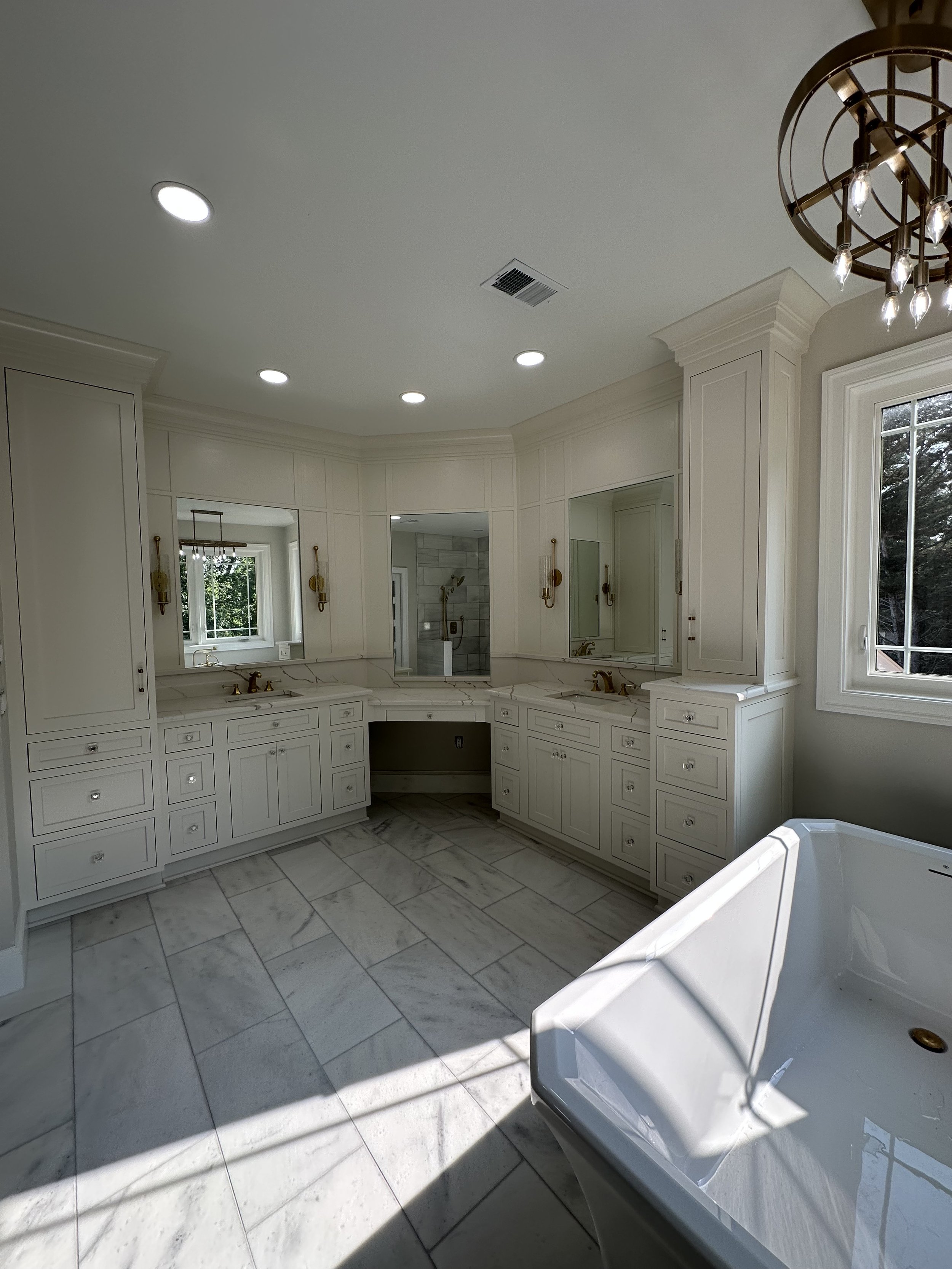 Luxury bathroom with white cabinetry, marble floors, a large window, and a bathtub in the foreground.