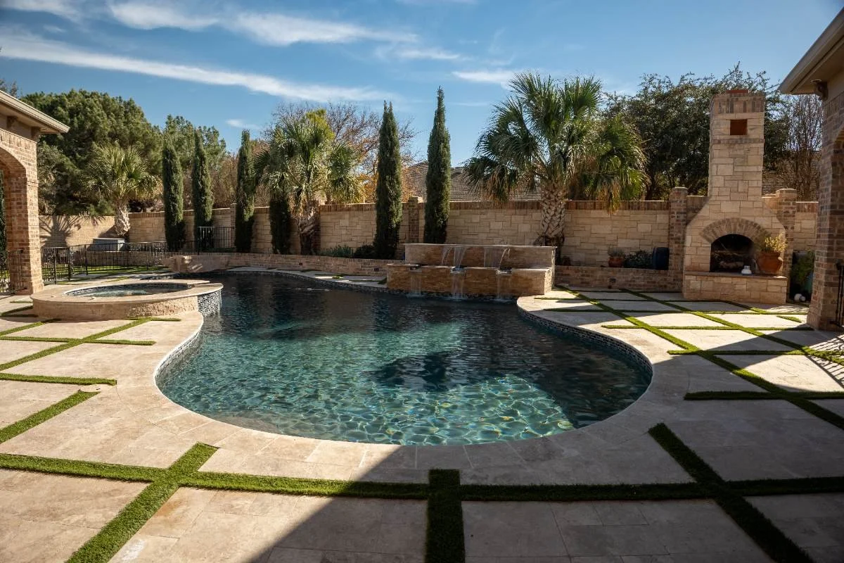 Curved pools & spas layout with rebuilt water feature wall and travertine hardscape in Andrews, TX