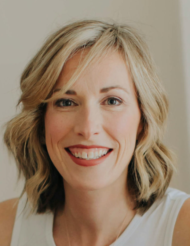 Close-up of a smiling woman with shoulder-length wavy blond hair, wearing a white sleeveless top.
