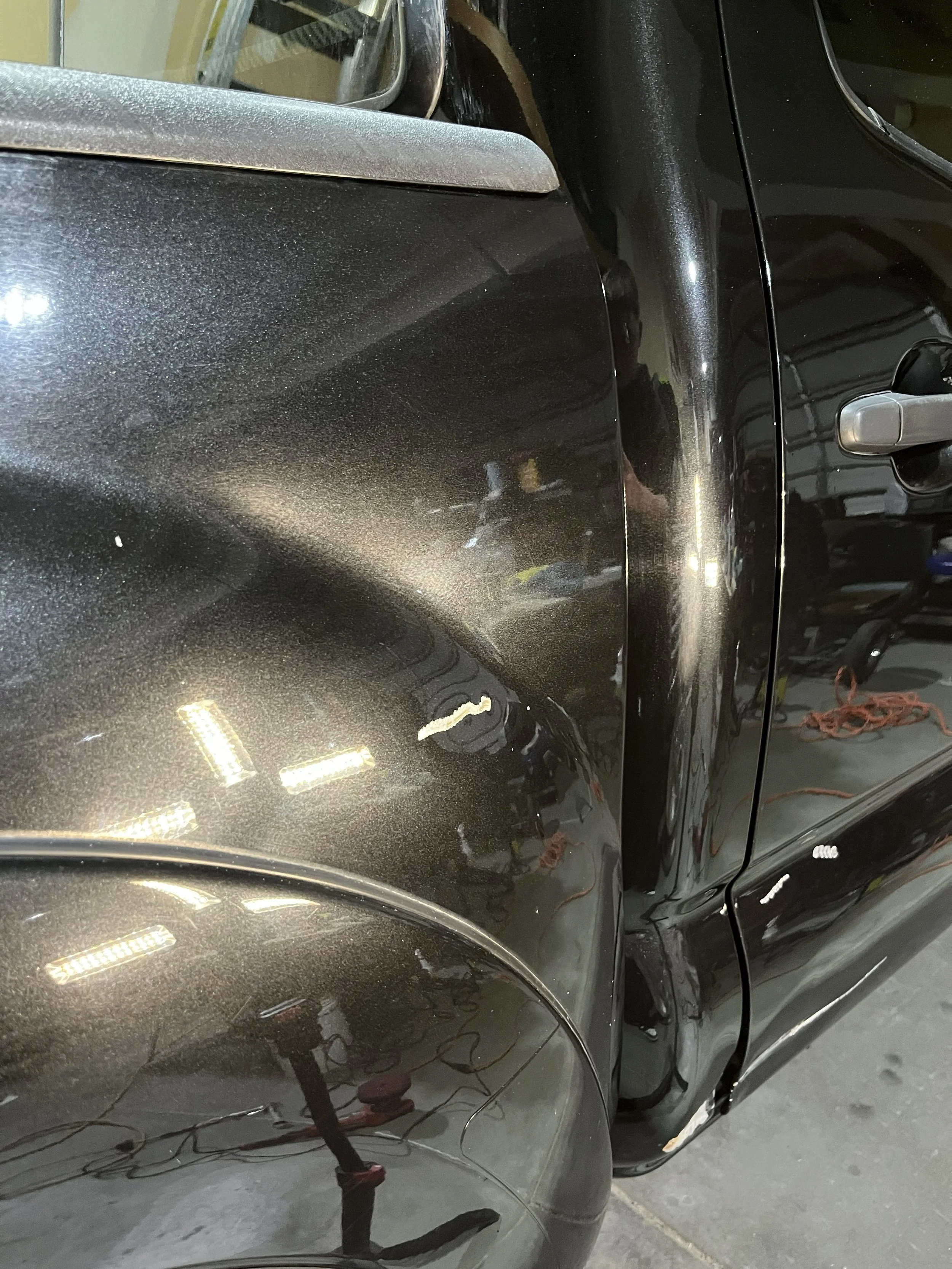 Close-up of a black car with reflections on its surface, parked in an indoor garage with overhead lighting.