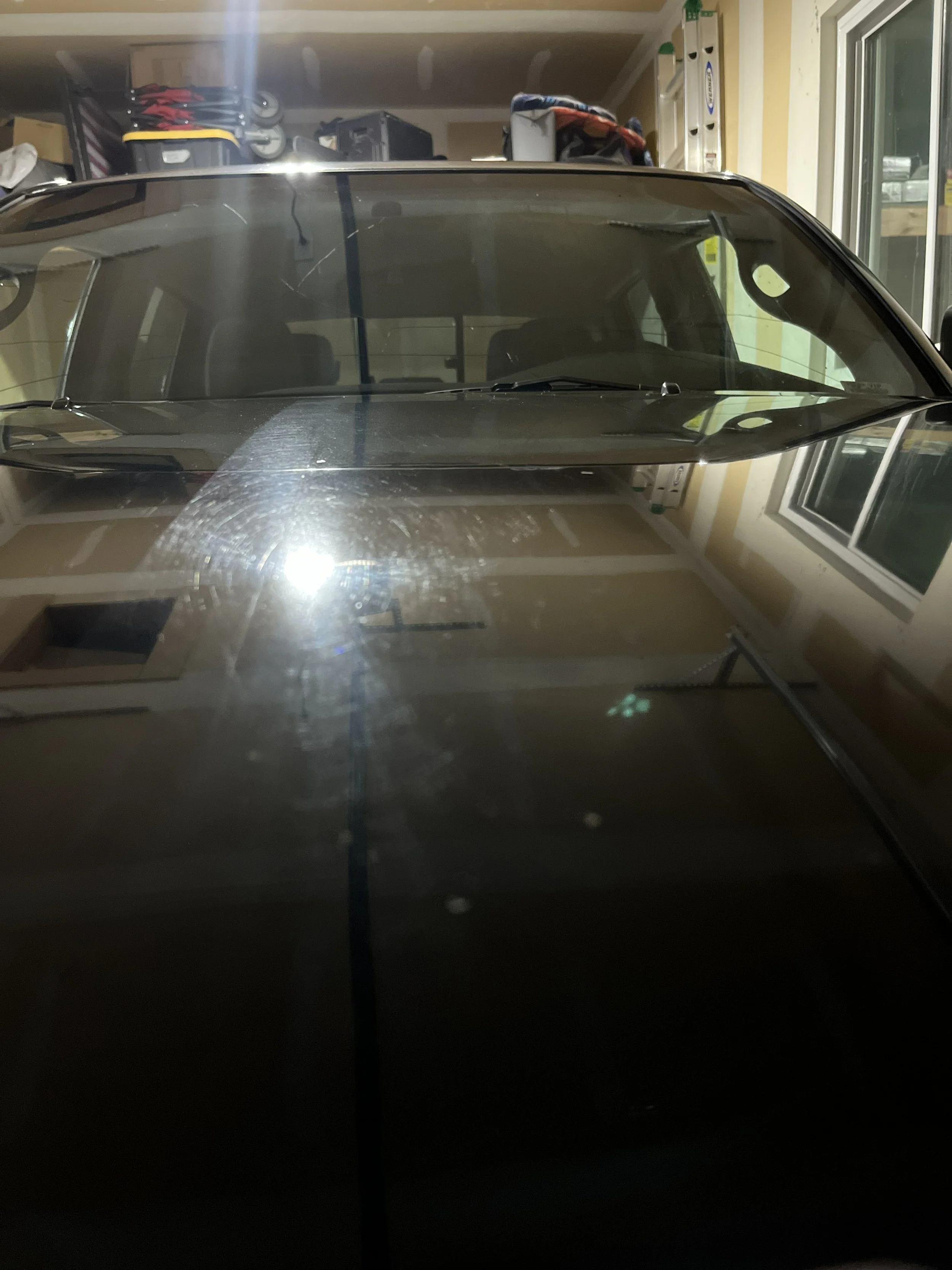 A black car parked in a garage with shelves, boxes, and a ladder visible in the background.