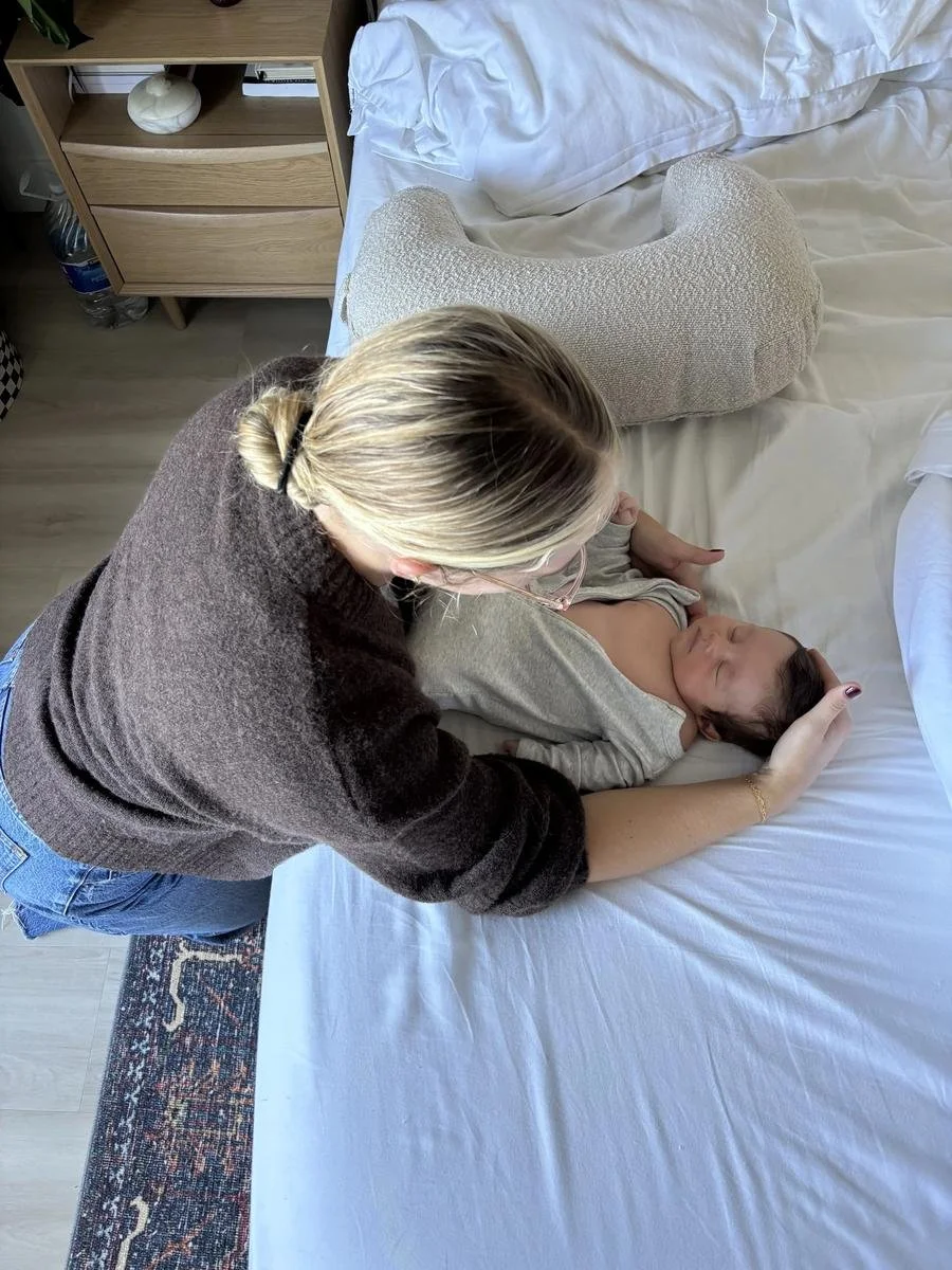 Dr Avonlea bending to soothe her sleeping newborn on the bed — Avonlea Brown Physical Therapy, Costa Mesa, CA.